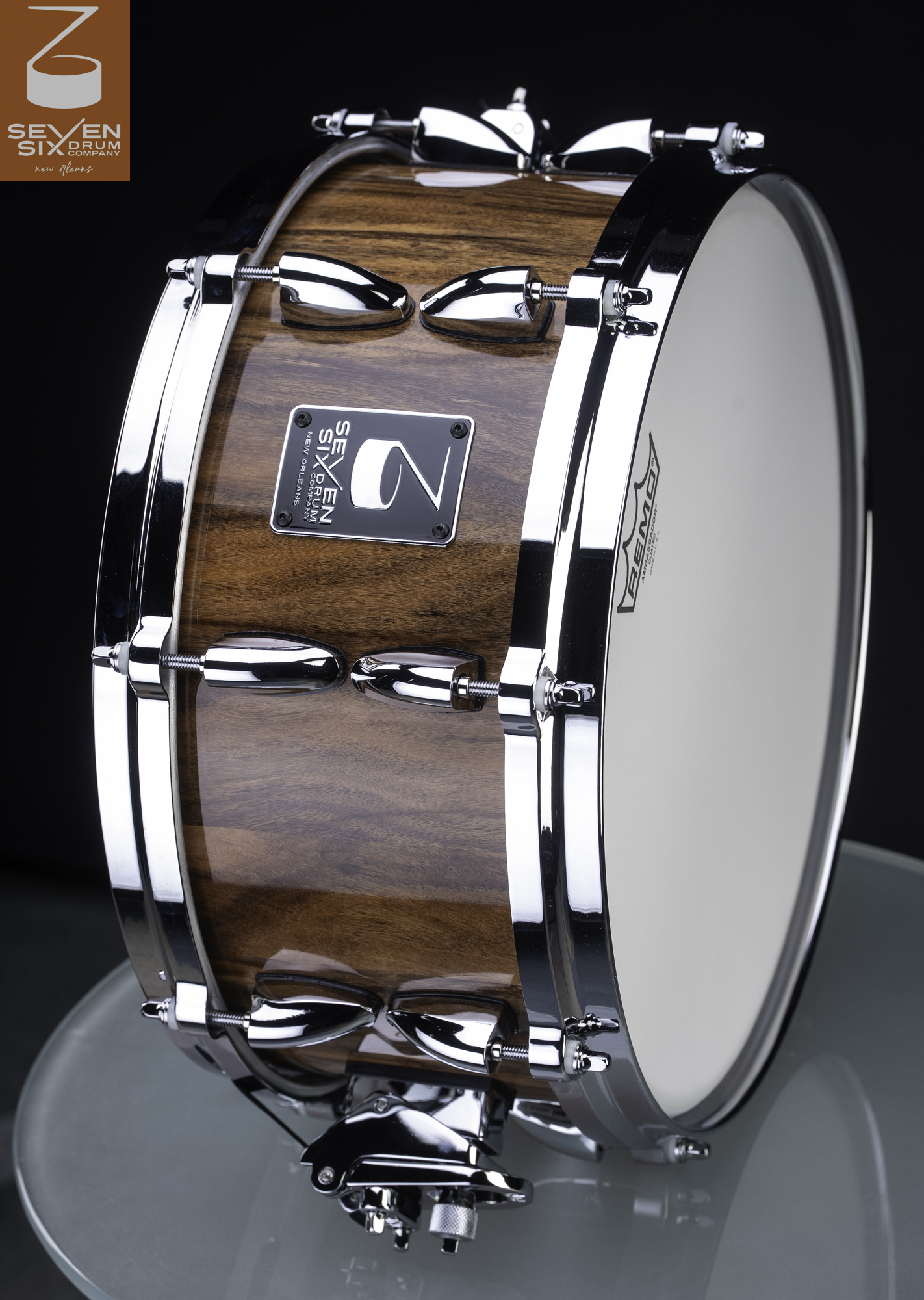 Handmade snare drum featuring a glossy brown wood shell, polished chrome lugs and hoops, and a white drumhead.