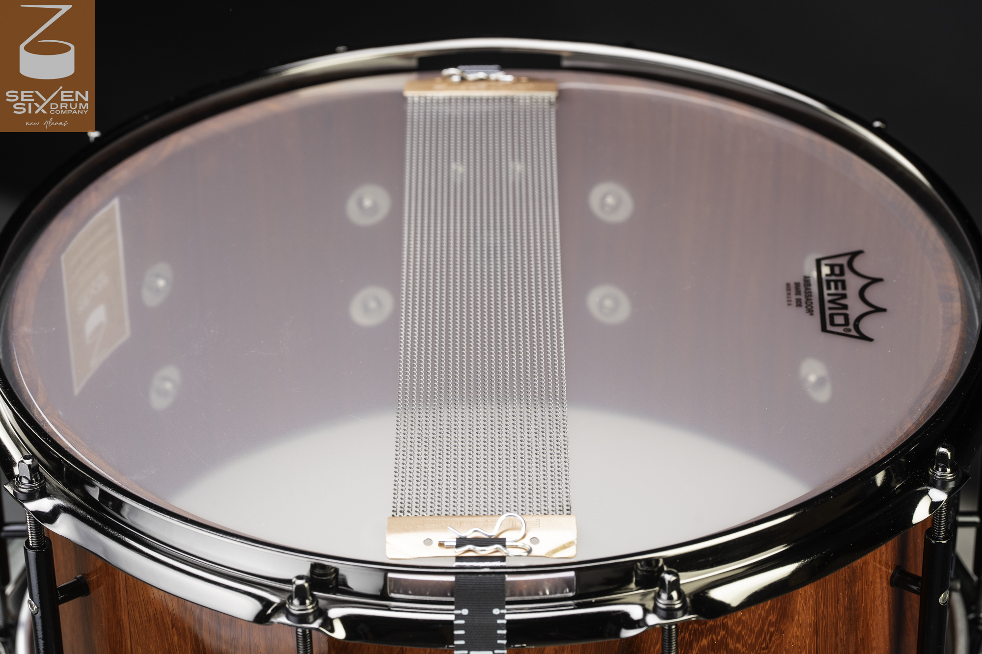 Snare drum bottom featuring a glossy red wood shell, chrome rim, clear head, and steel snare wires with copper end plates.