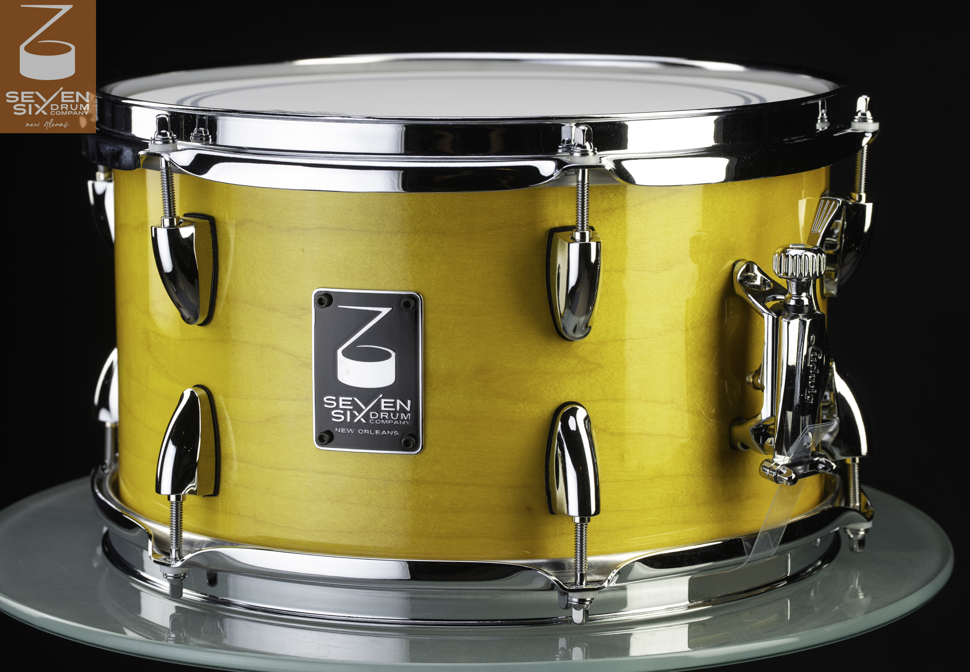 Snare drum with a glossy yellow wood shell, polished chrome hoops, dual bullet lugs, and a side-mounted throw-off.