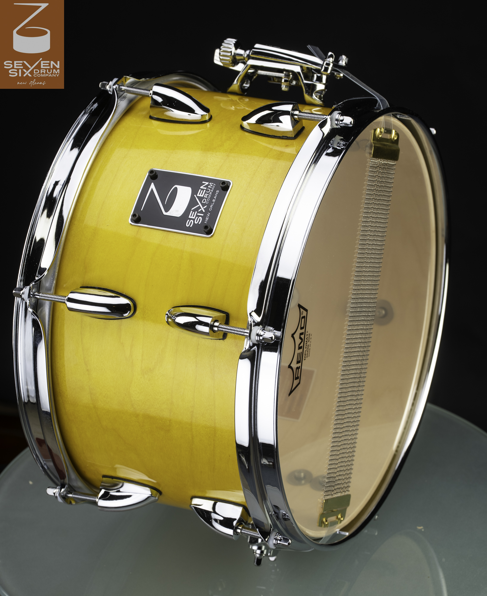 Handmade snare drum with a gloss yellow wood finish, chrome hoops and lugs, and snare wires against a clear resonant head.