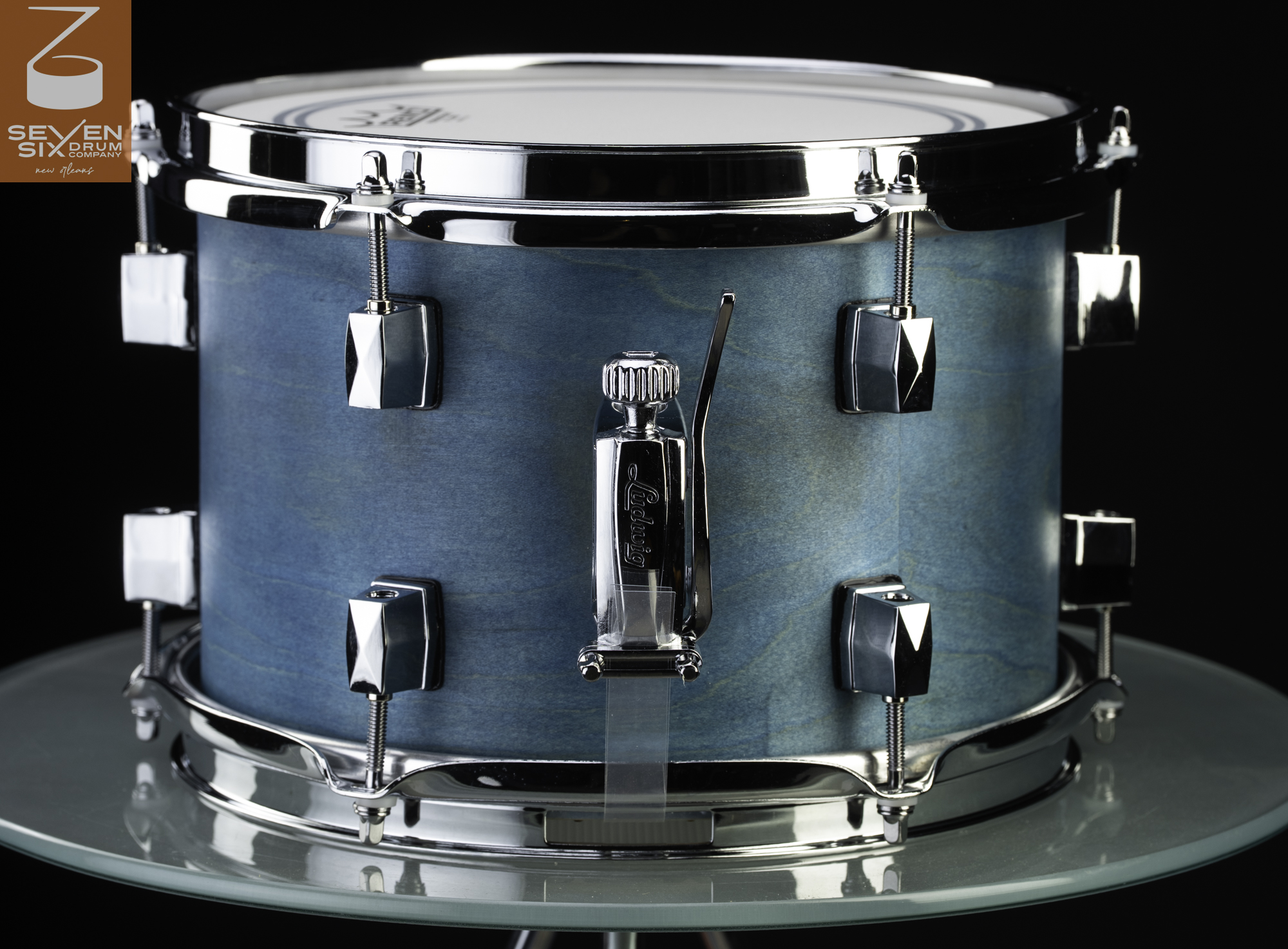 Handmade wooden snare drum with a light blue stain finish, chrome hoops, lugs, and a Ludwig throw-off.