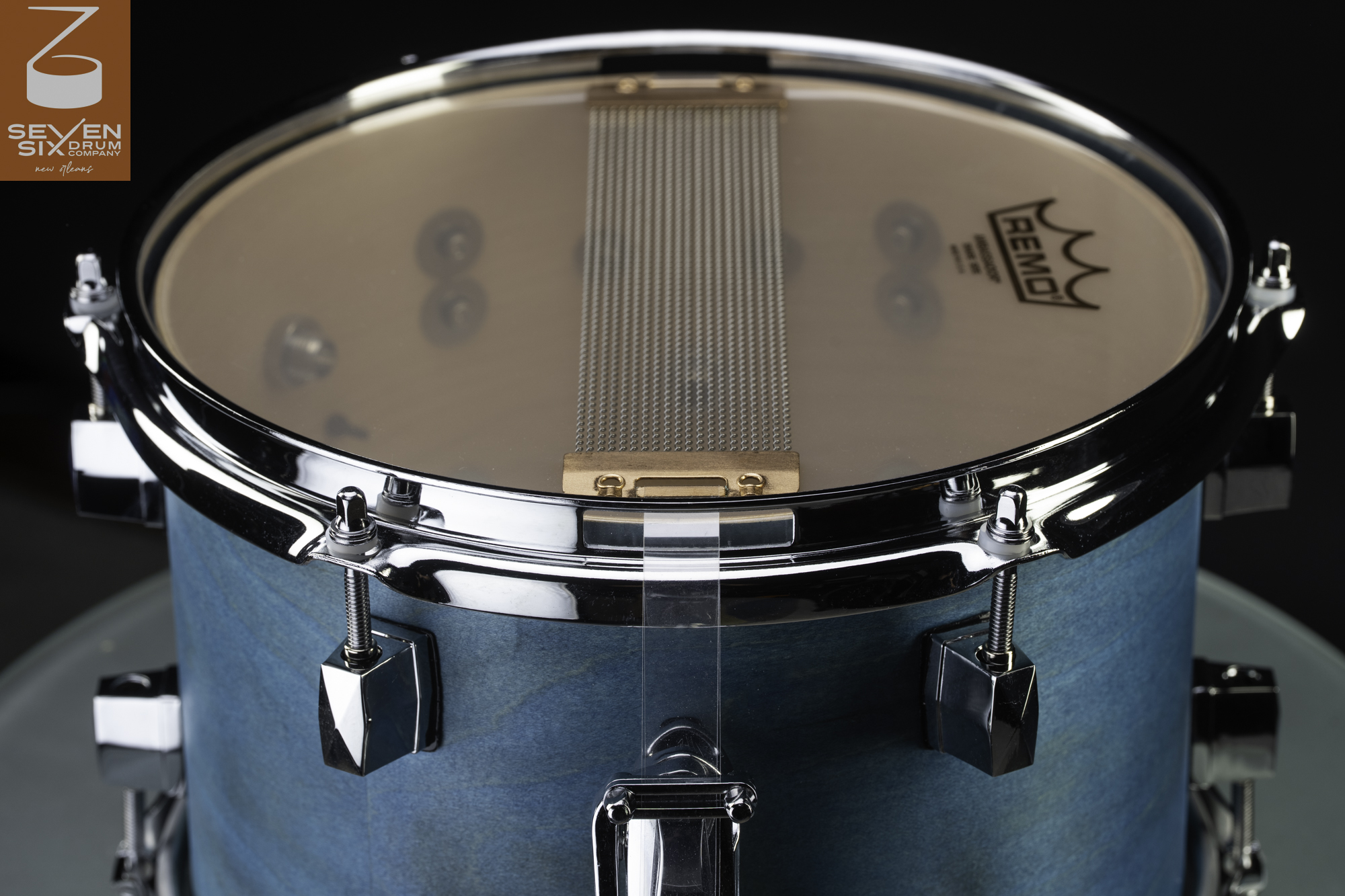Teal-stained wood snare drum showing chrome hardware and snare wires across a Remo resonant head.