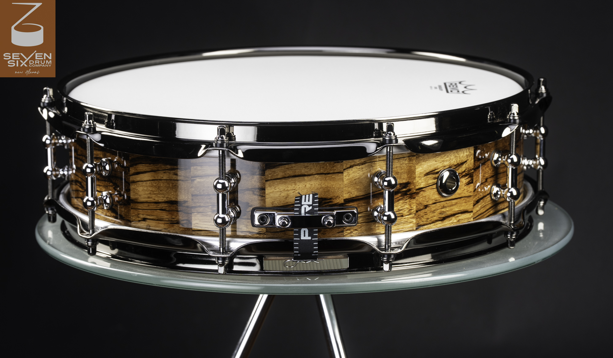Handmade snare drum featuring a glossy segmented wood shell with polished chrome tube lugs and hoops.
