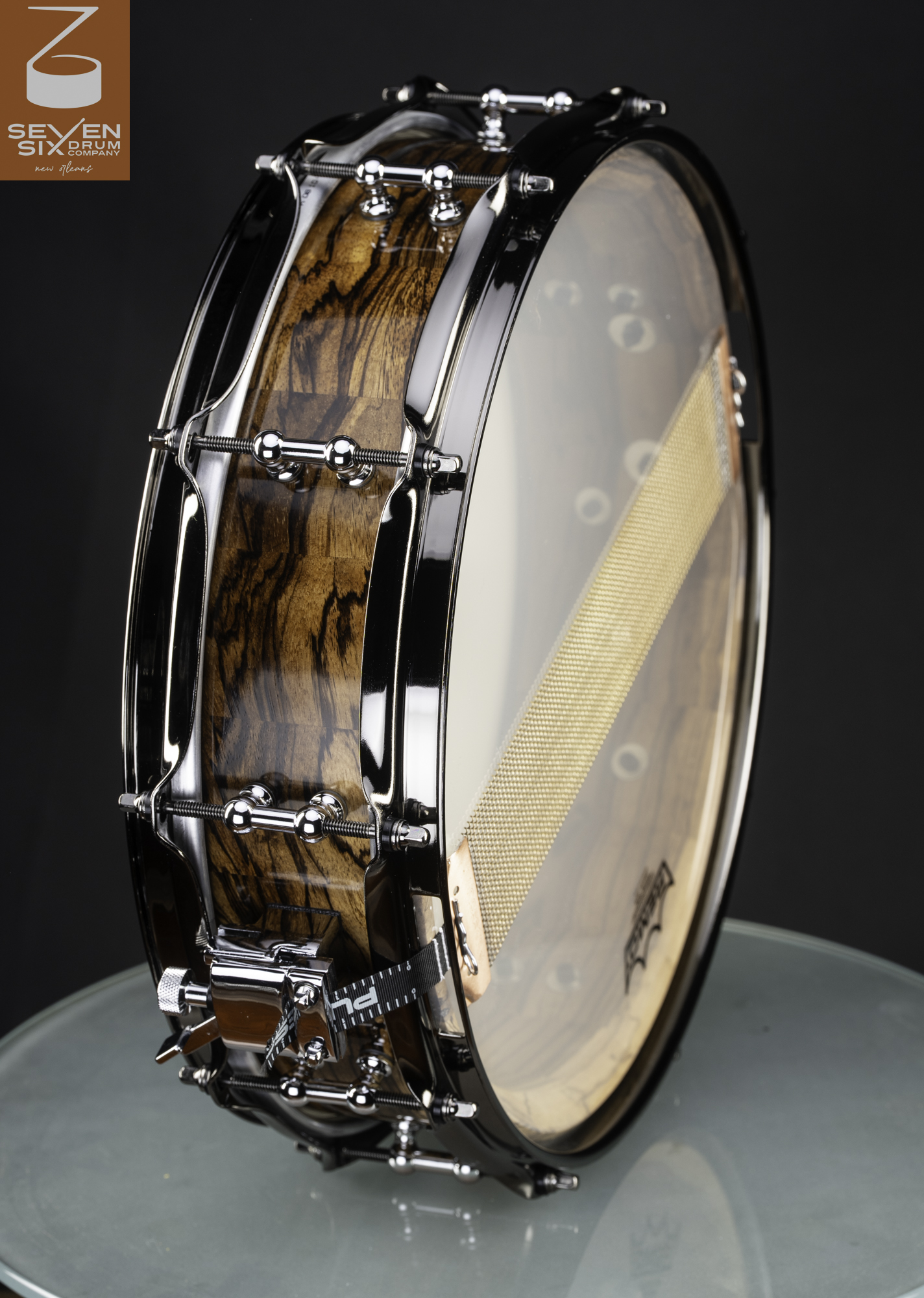 Handmade snare drum featuring a glossy striped wood shell, chrome tube lugs, black nickel hoops, and bottom snare wires.
