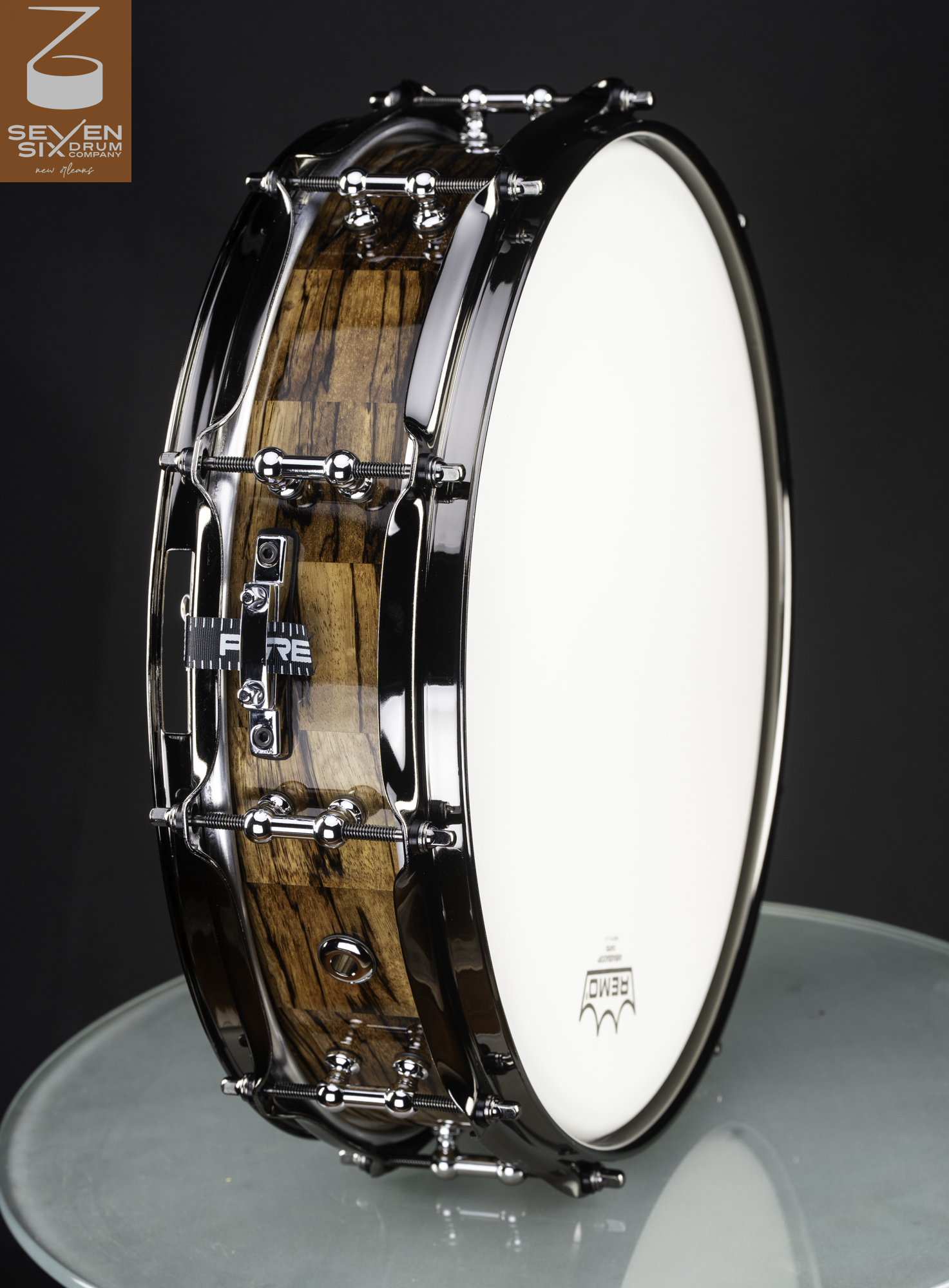 Handmade snare drum with a high-gloss figured wood shell, black nickel hoops, and chrome tube lugs.