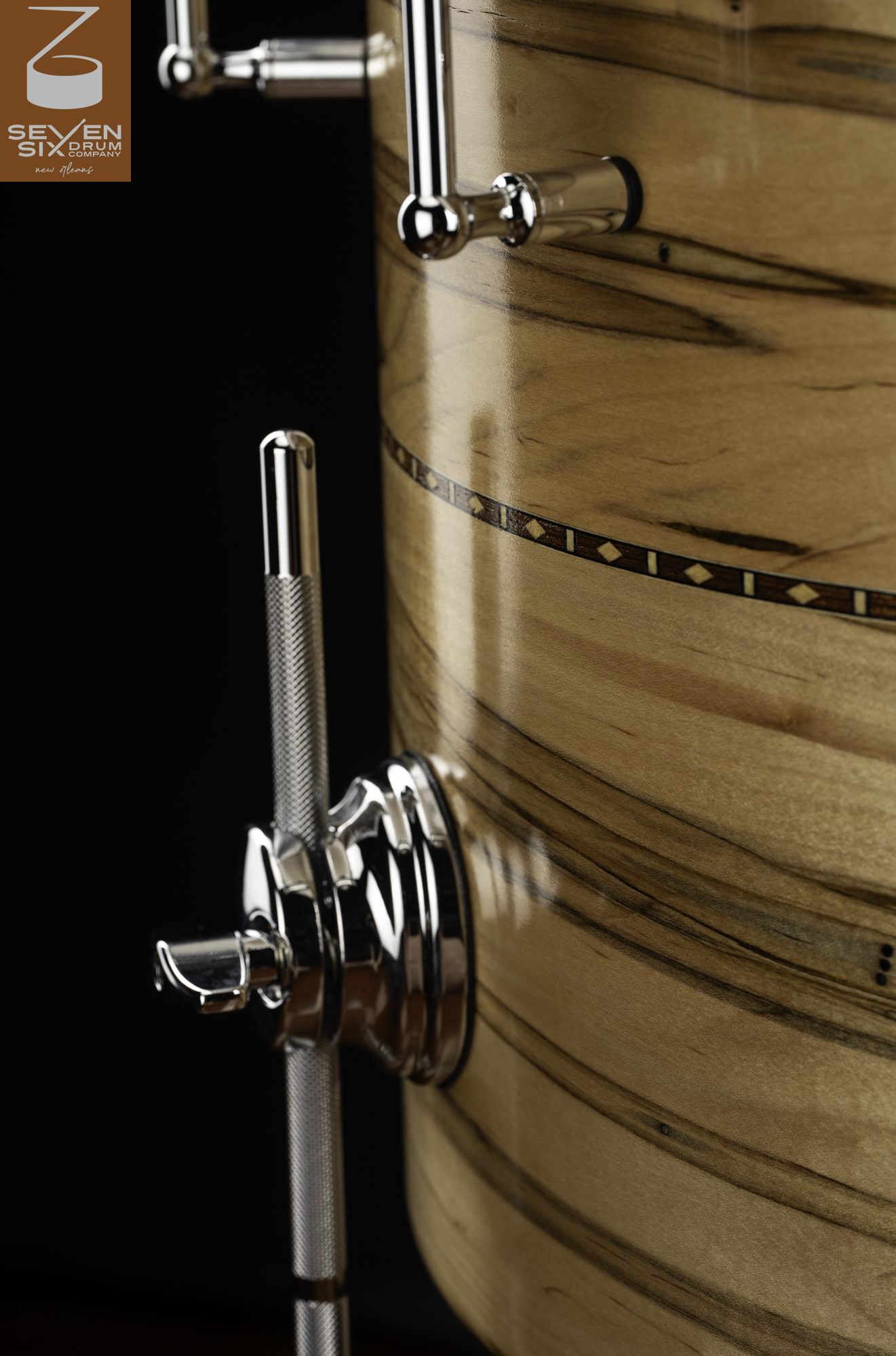 Glossy natural-finish wood drum shell featuring an inlay band and a chrome floor tom leg bracket with a knurled leg.