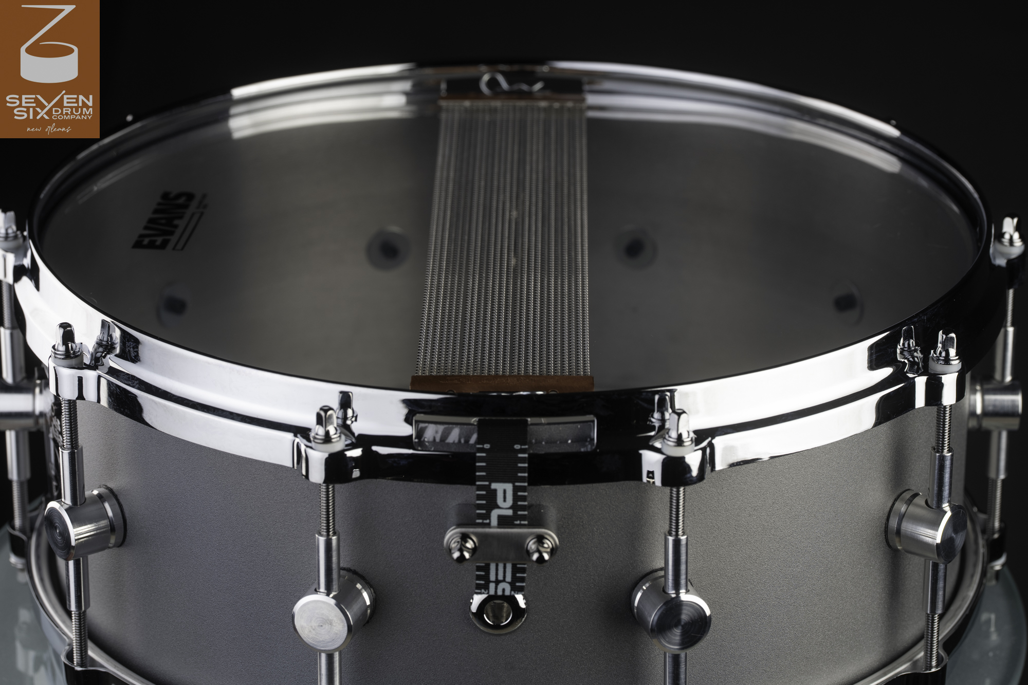 Snare drum with a matte gray metal shell, polished chrome hoop, wire snares, and machined cylindrical lugs.