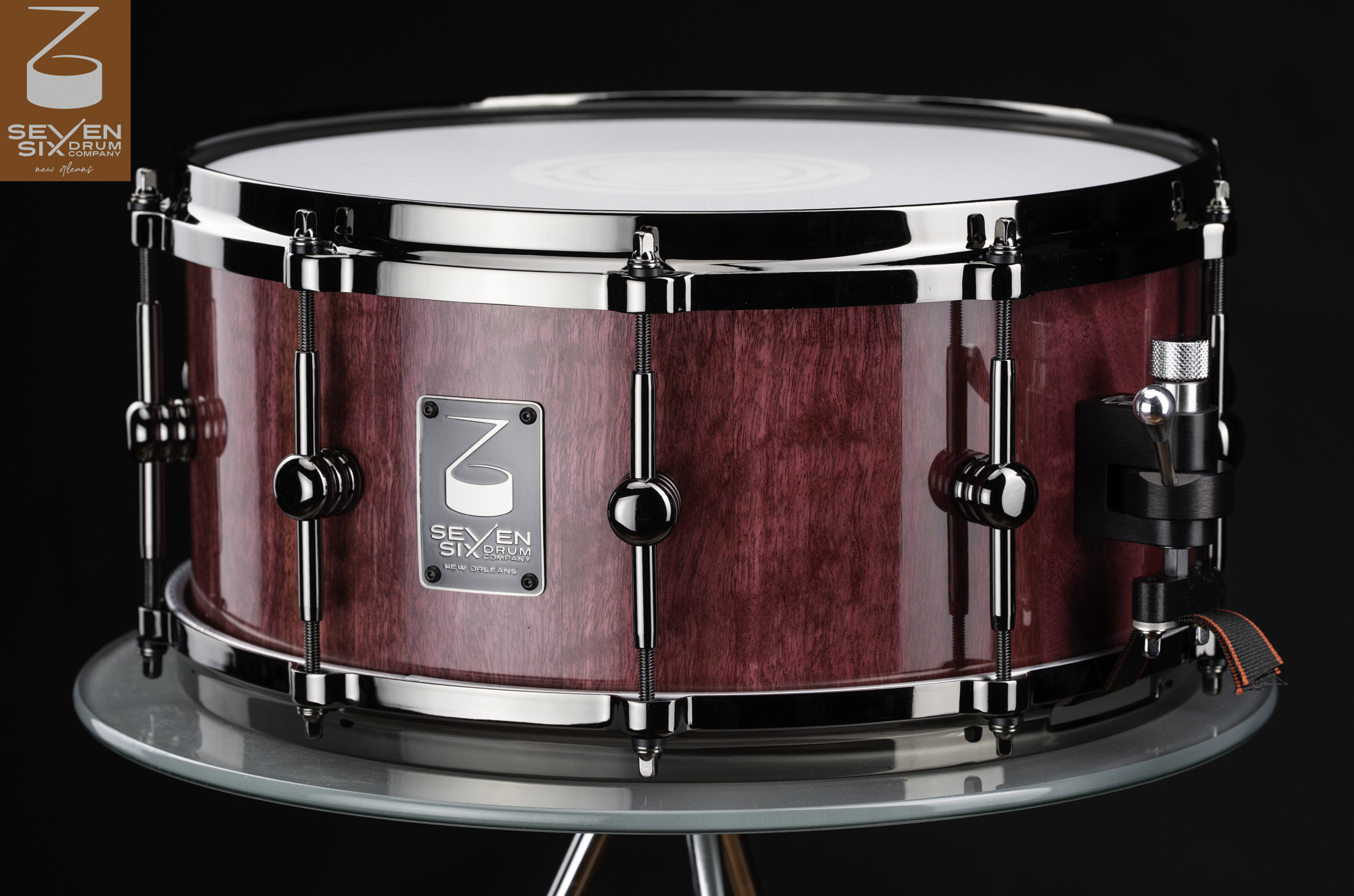 Handmade snare drum with a gloss purple wood grain shell, black nickel hardware, and center-mounted tube lugs.