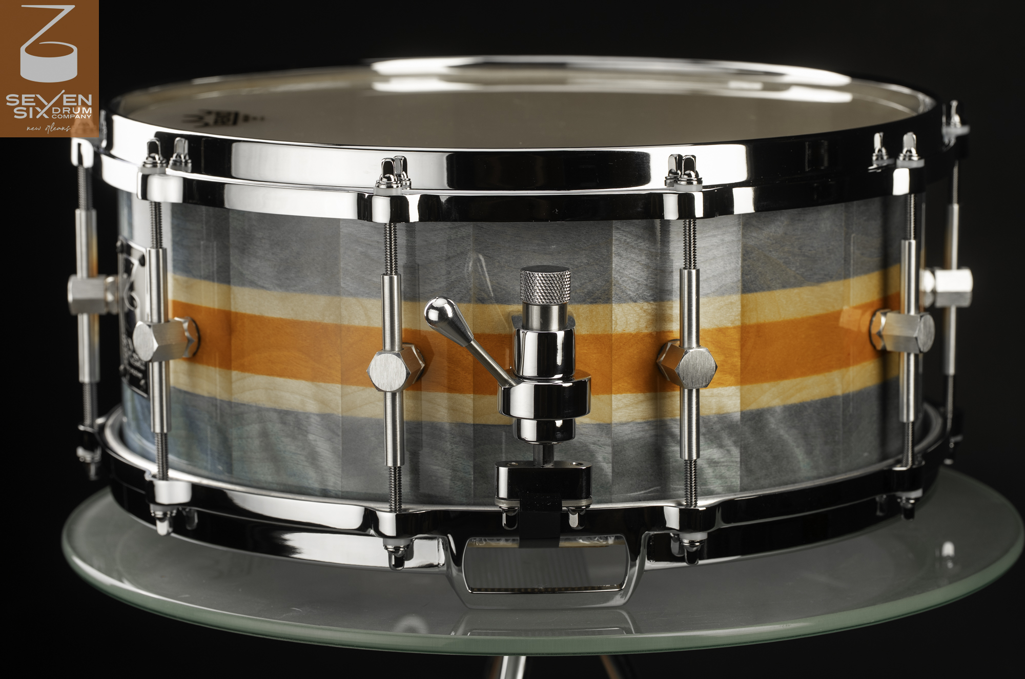 Handmade wood snare drum with blue-gray and orange stripes, featuring polished chrome hoops and a snare throw-off.