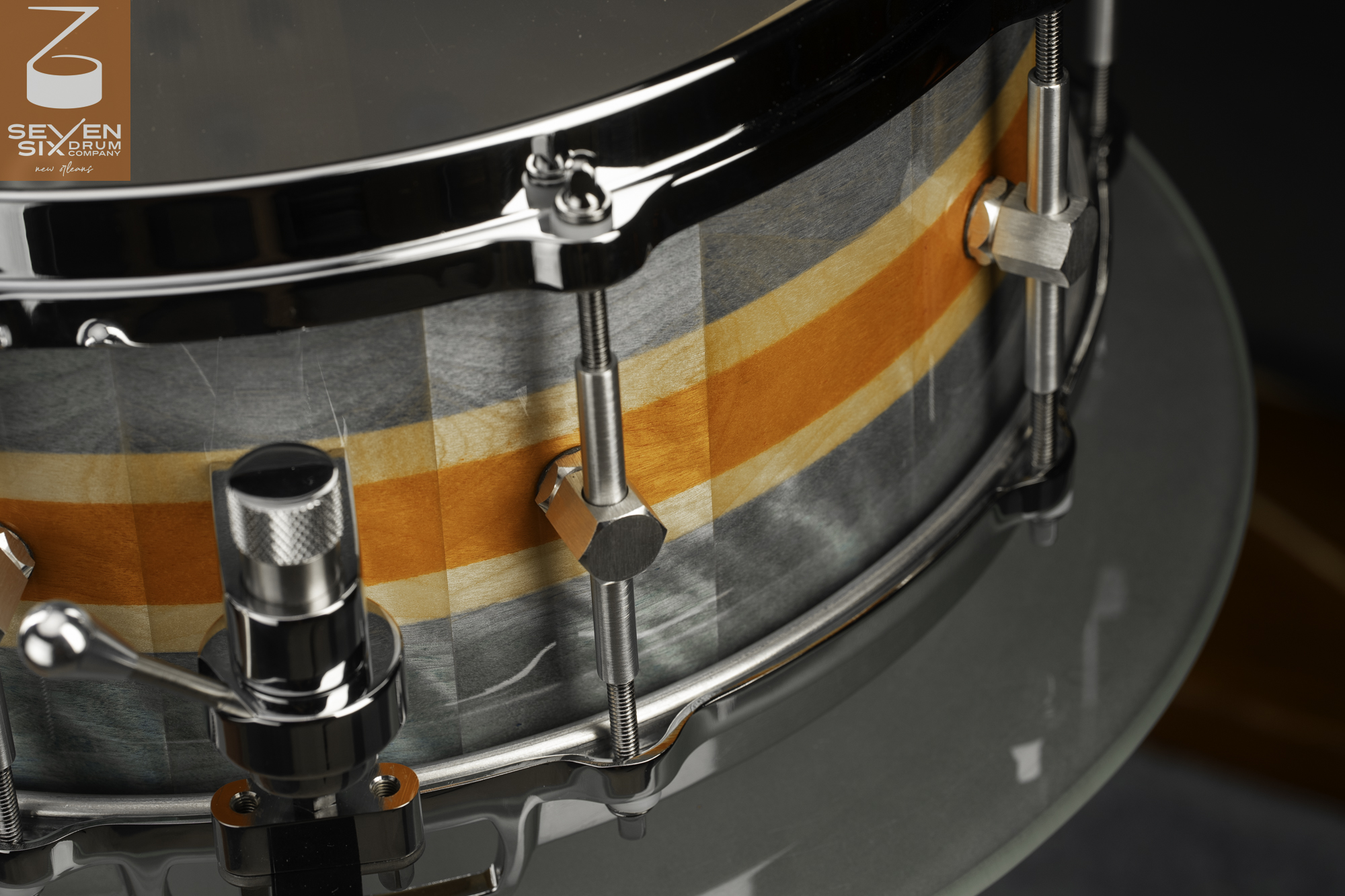 Handmade snare drum with a gray and orange striped wood shell, chrome hoops, hex lugs, and a snare throw-off.