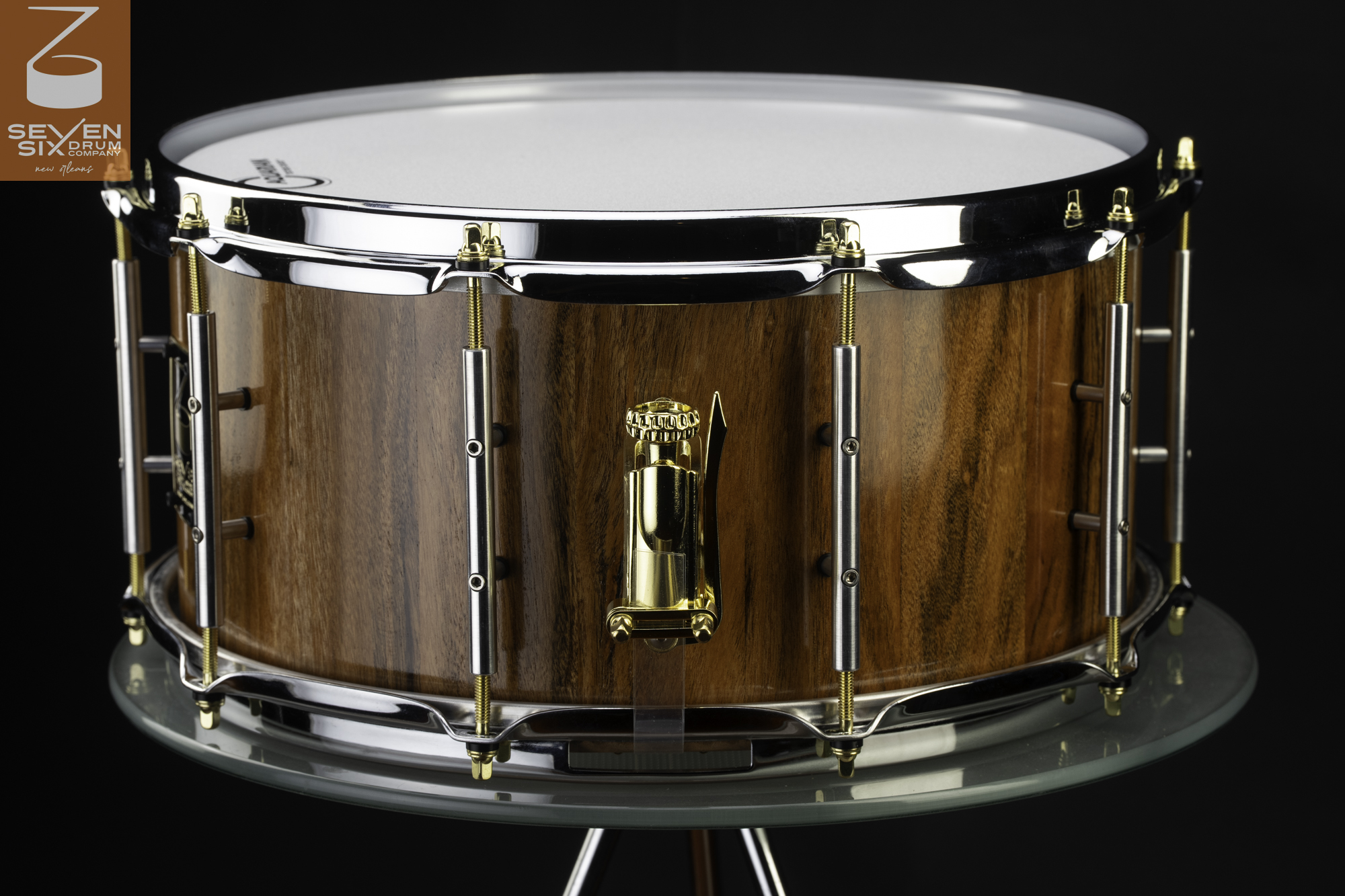 Handmade snare drum with a glossy natural wood shell, chrome hoops, dual-tone tube lugs, and a polished gold strainer.