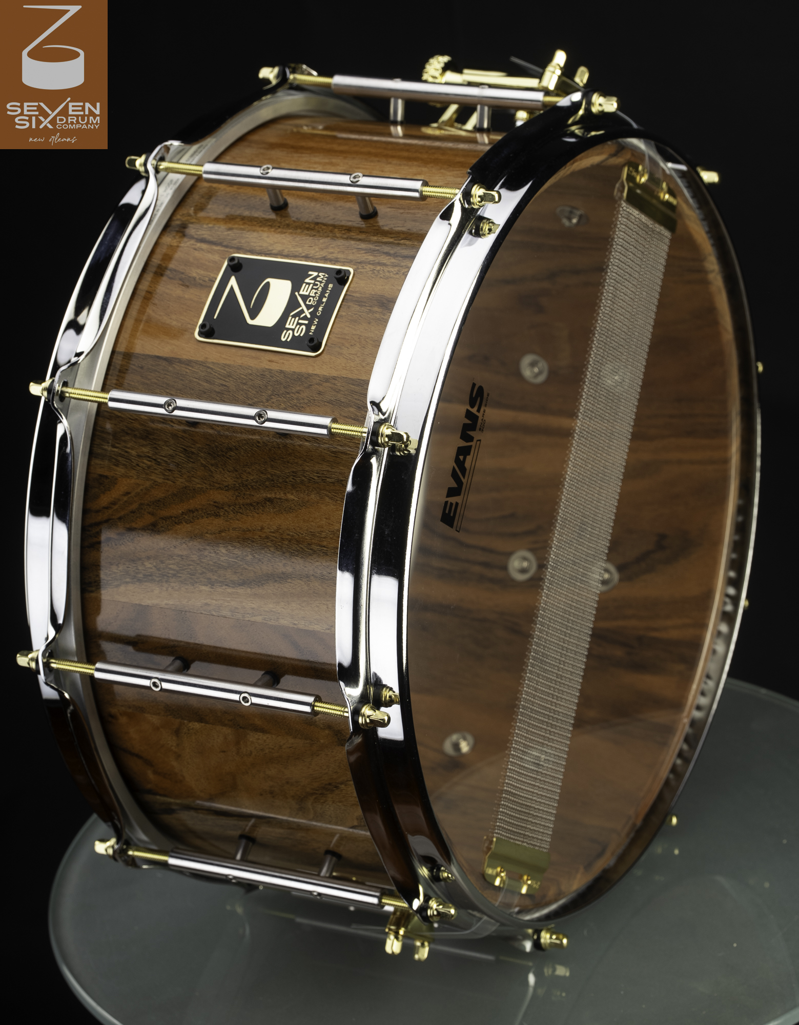 Glossy wood grain snare drum fitted with chrome hoops, tube lugs, and gold tension rods.