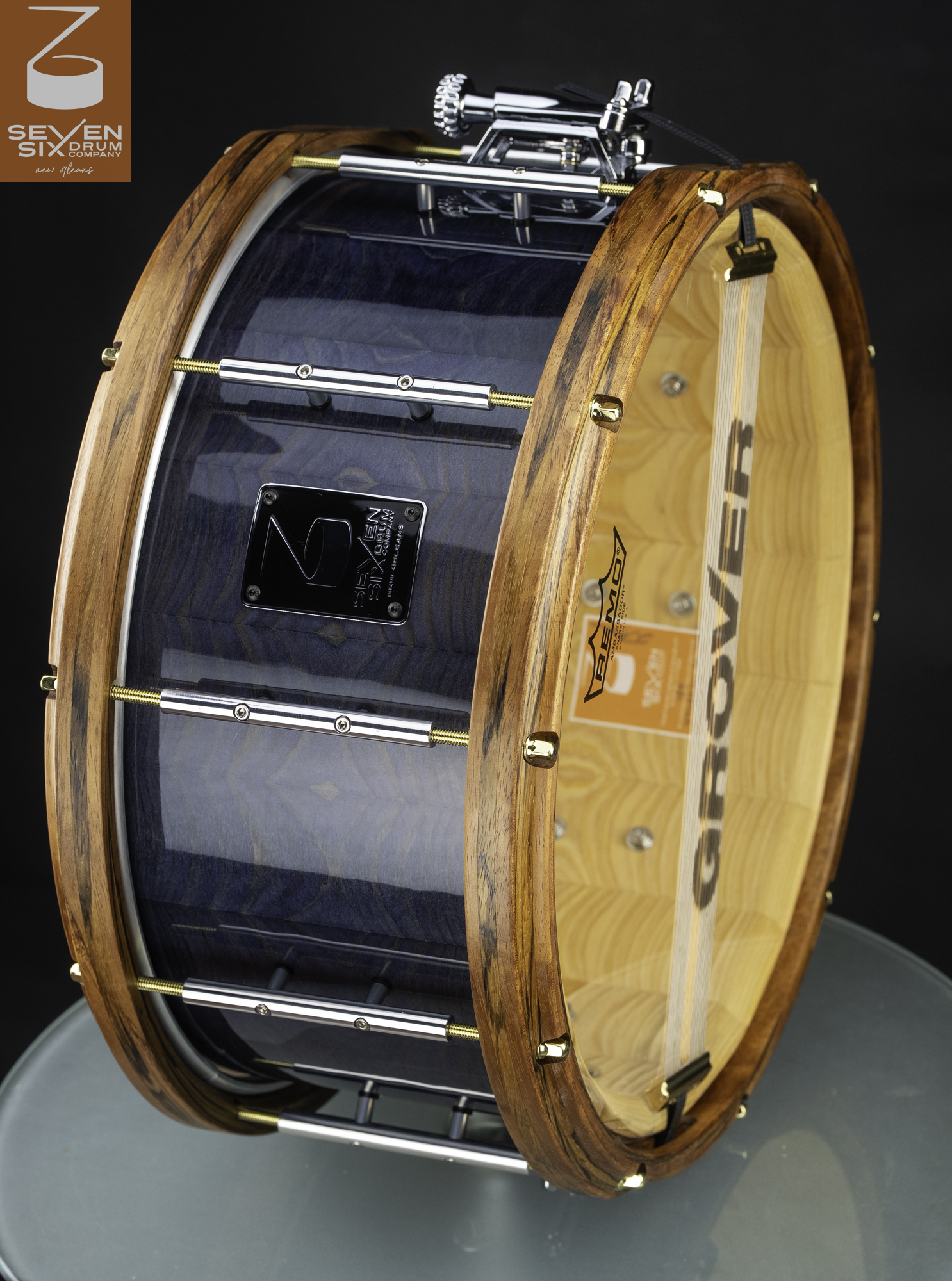 Handmade snare drum featuring a glossy blue wood shell, natural wood hoops, chrome tube lugs, and brass tension rods.