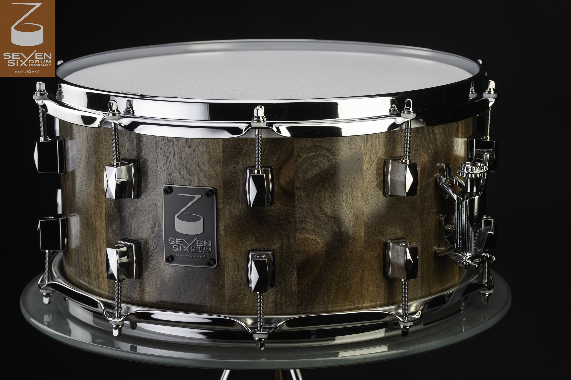 Handmade walnut stave snare drum with a natural finish, polished chrome hoops and lugs, and a black badge.