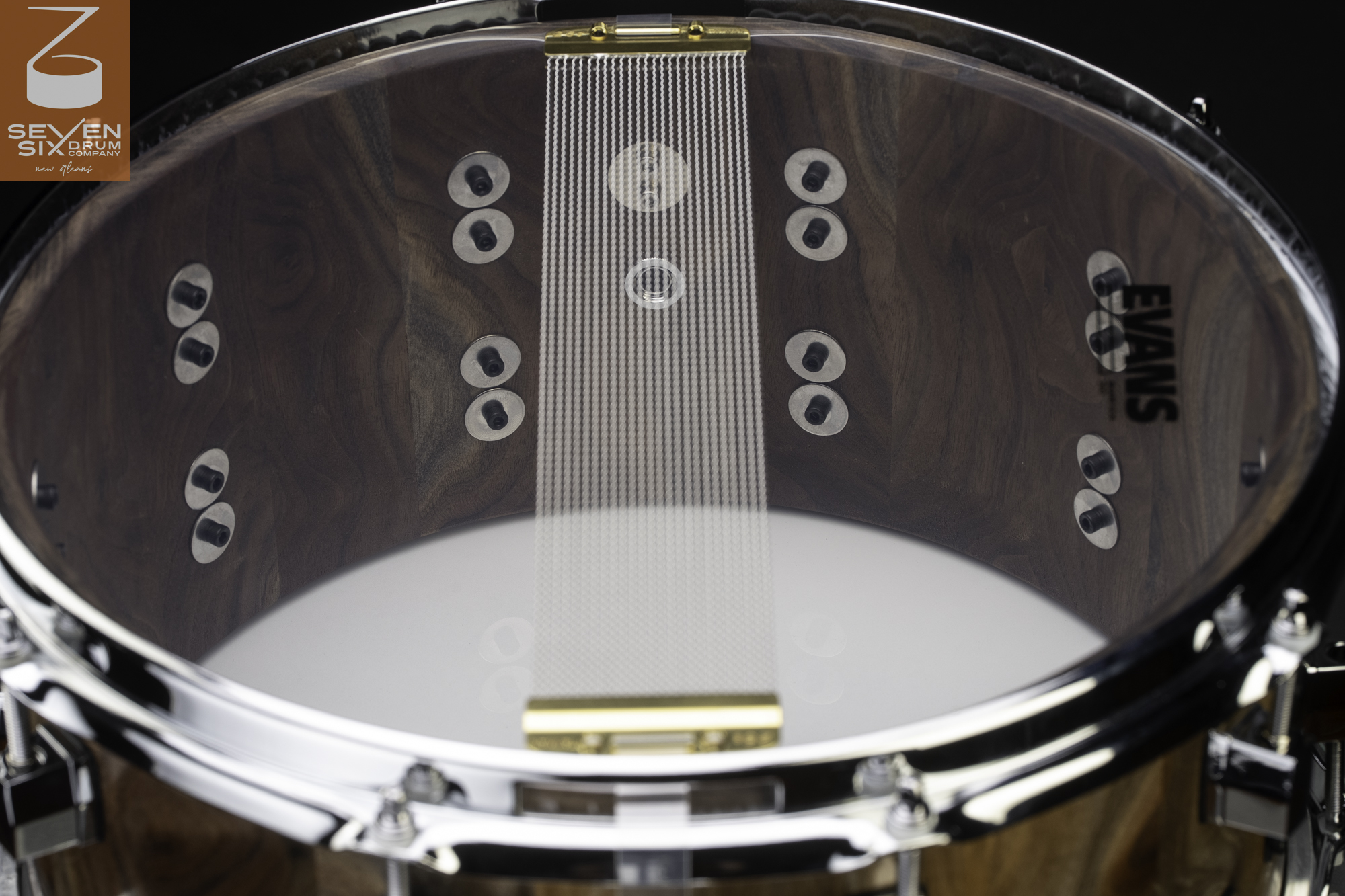 Interior of a natural dark walnut snare drum featuring chrome hoops, internal lug screws, and snare wires with brass clips.