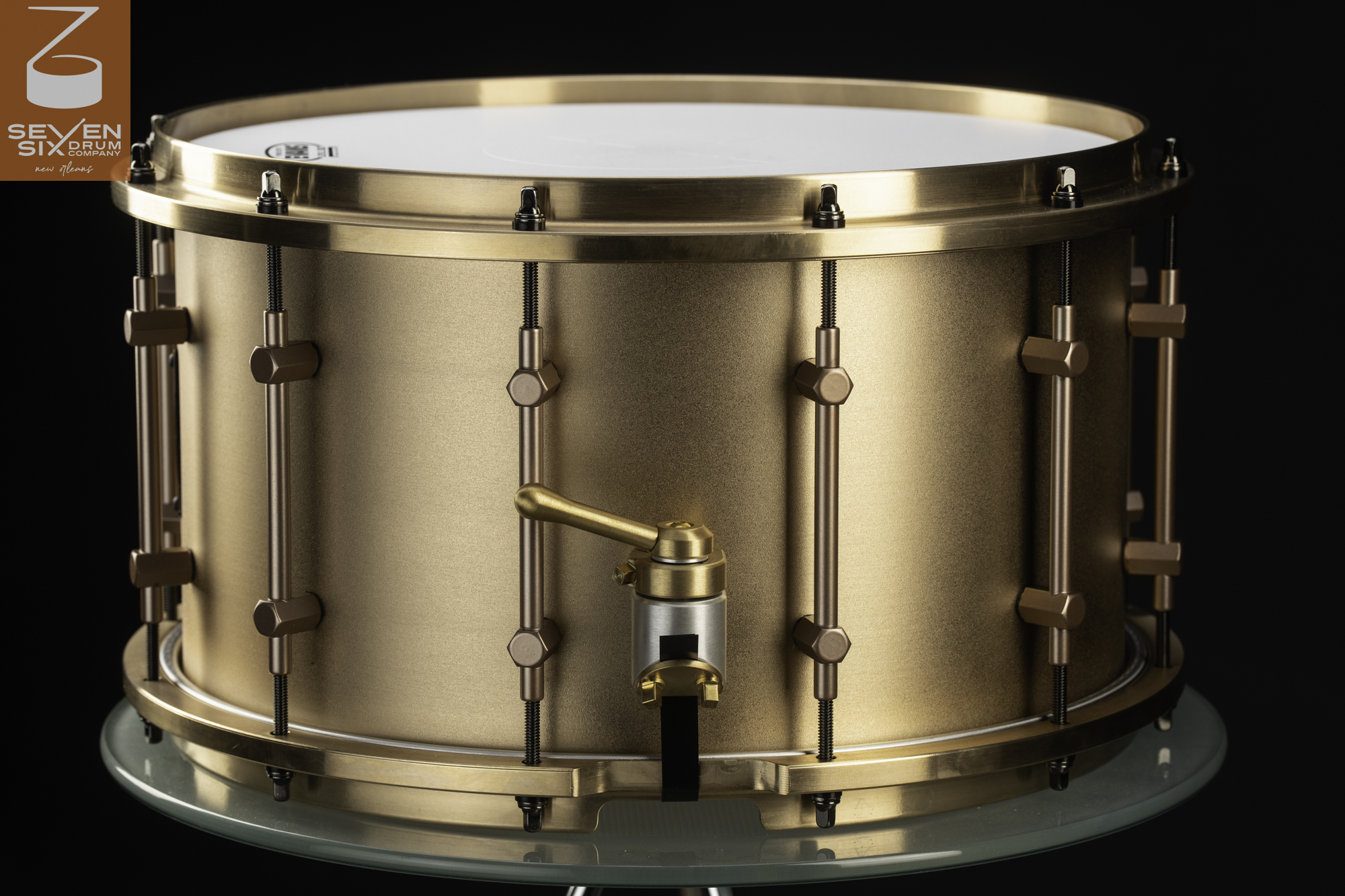 Brushed bronze snare drum featuring matching metal hoops, tube lugs, and a machined lever throw-off.