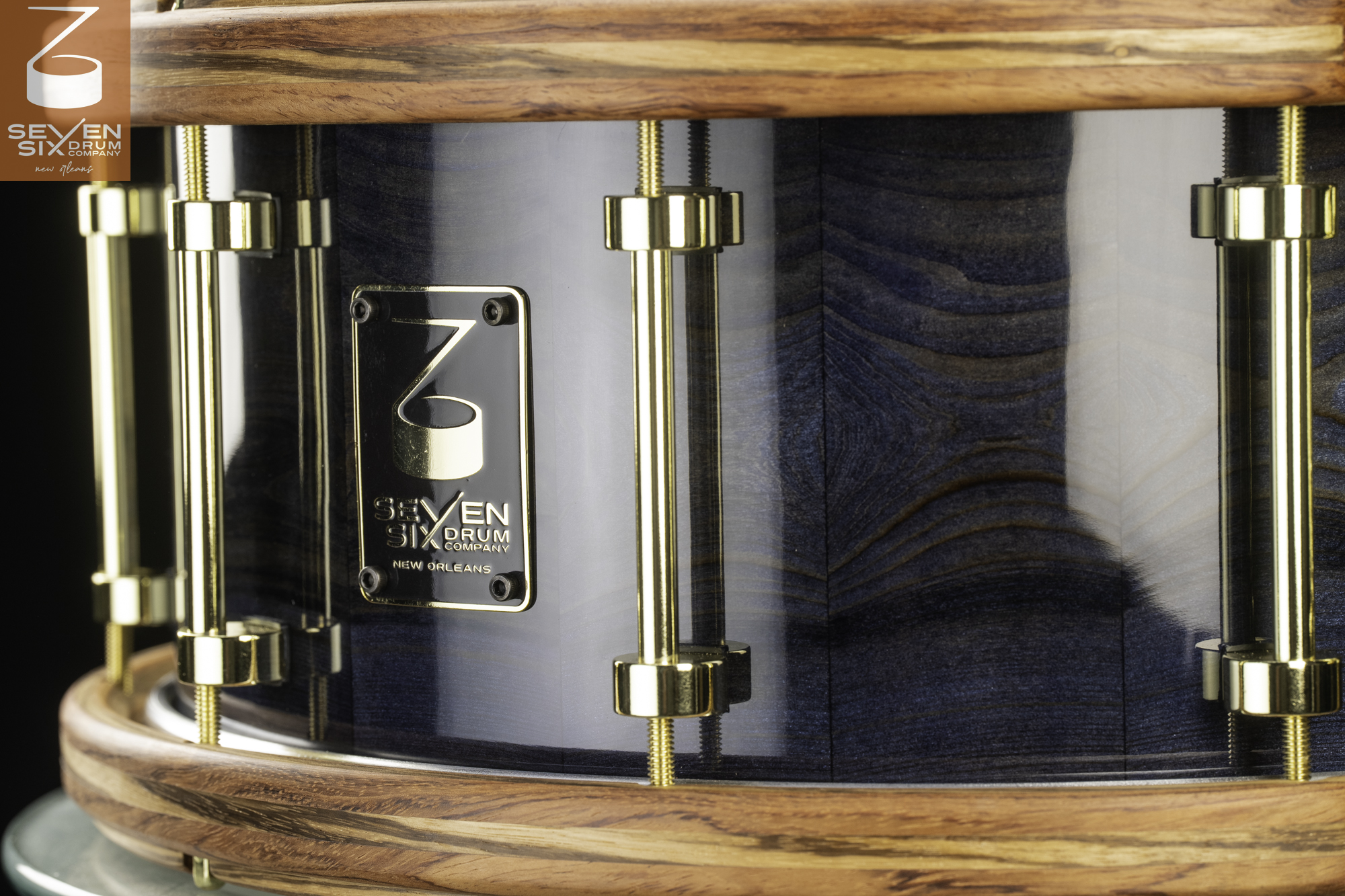 Snare drum featuring a glossy blue wood grain shell, natural wood hoops, and polished brass tube lugs.