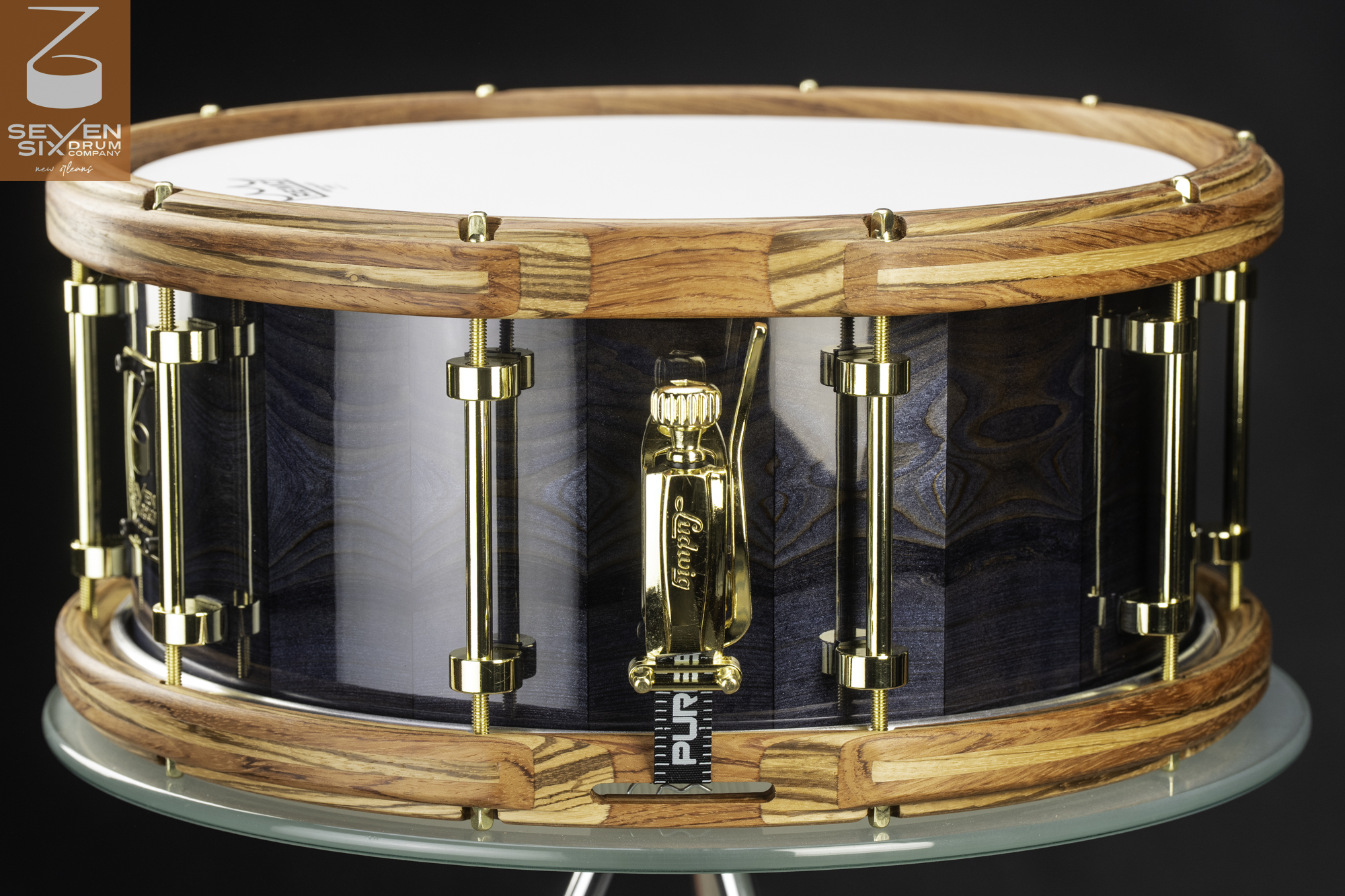 Glossy dark blue wood snare drum with segmented wood hoops and polished gold tube lugs and throw-off.