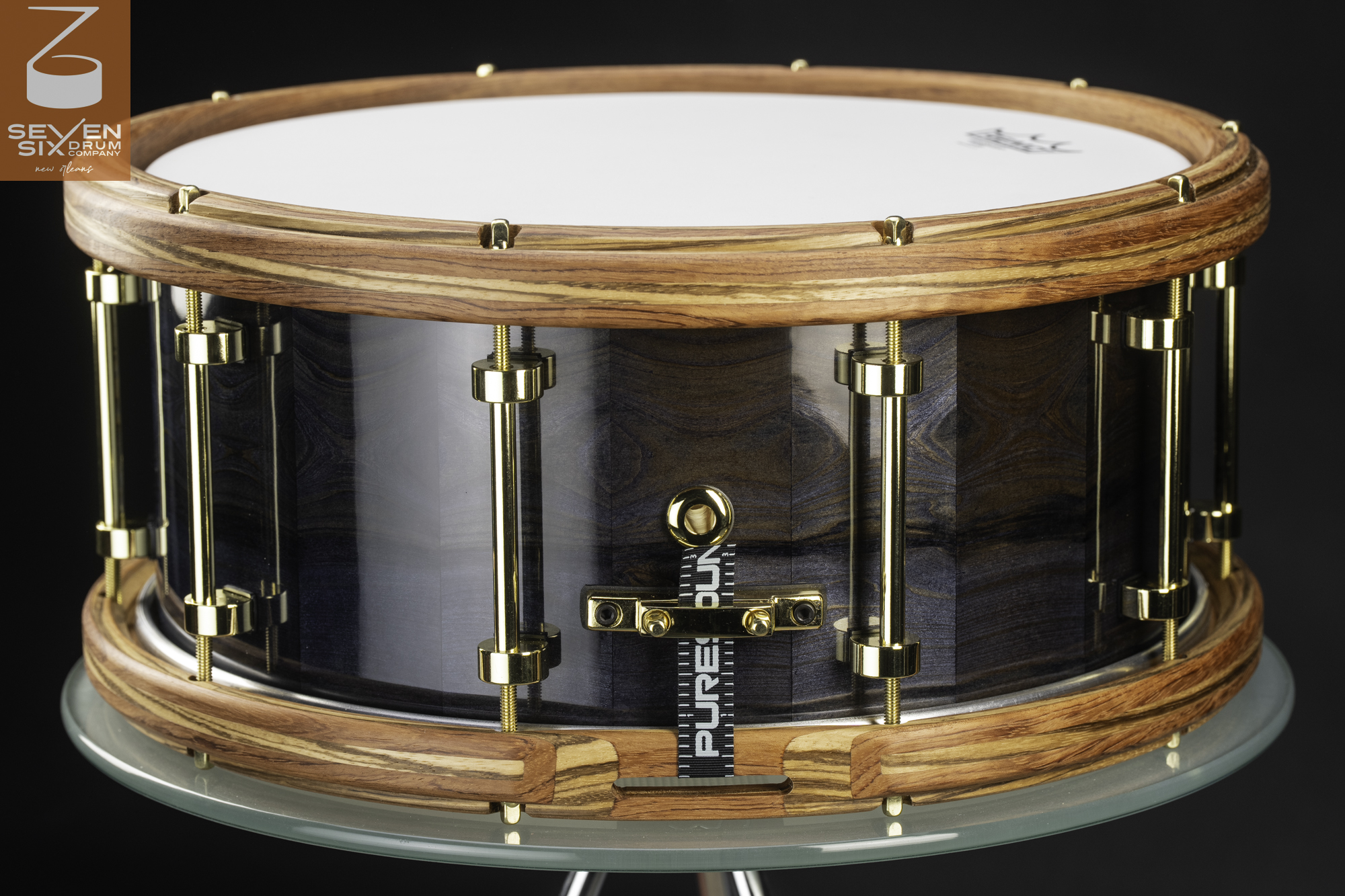 Handmade snare drum featuring a glossy blue wood shell, natural striped wood hoops, and polished gold tube lugs.
