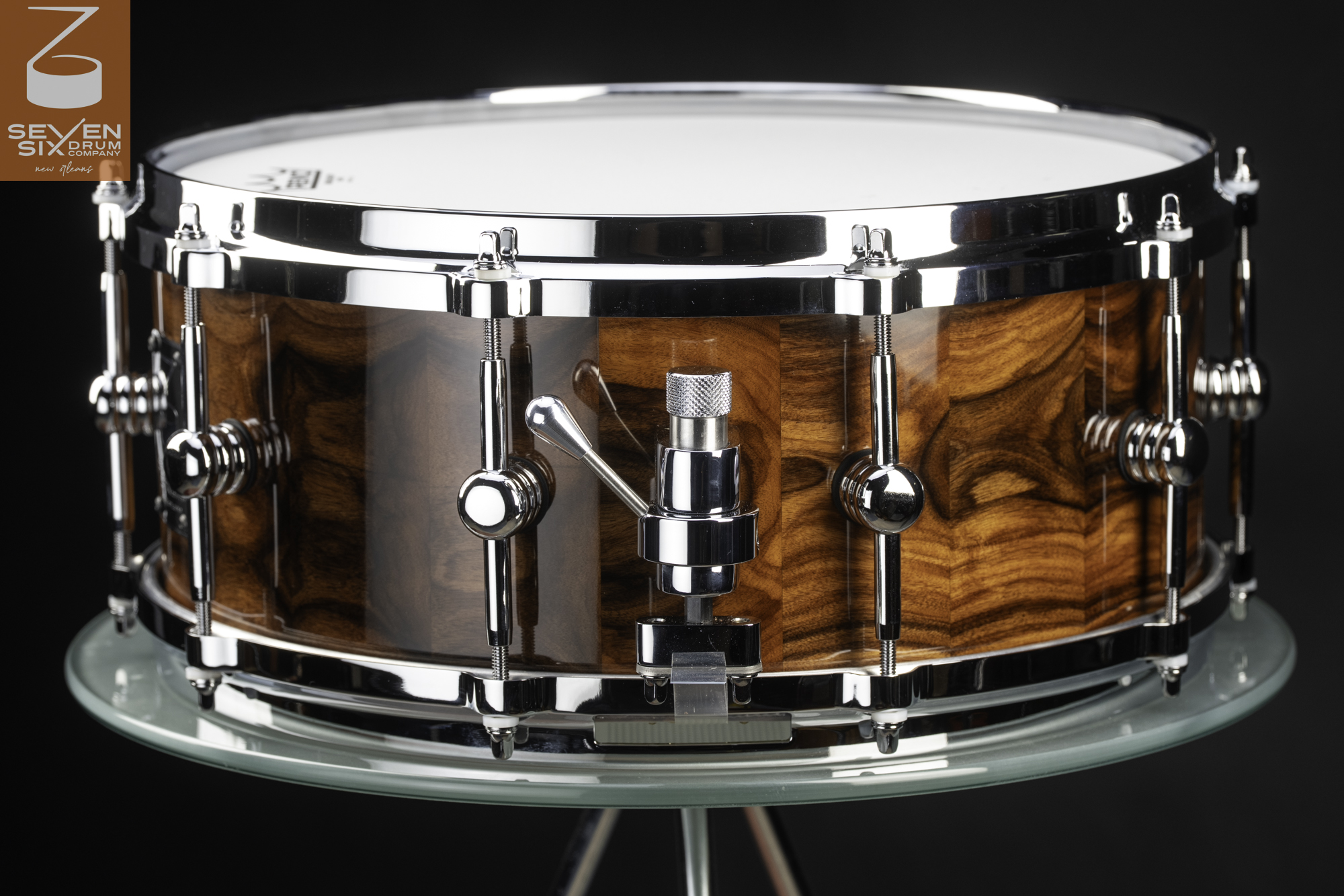 Snare drum featuring a glossy figured wood shell, polished chrome hoops, single-point lugs, and a snare throw-off.