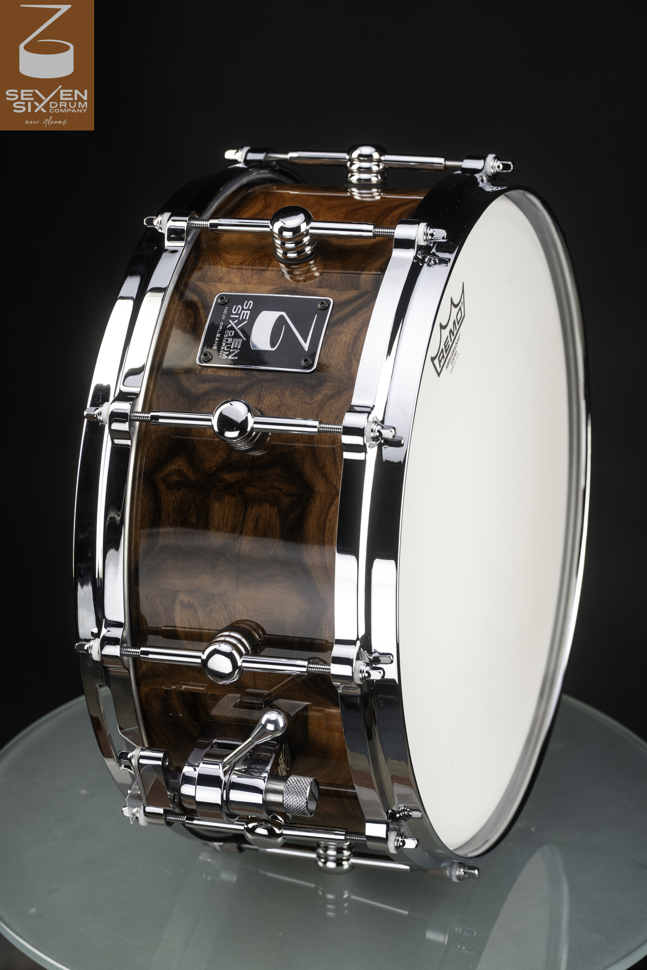 Handmade snare drum featuring a glossy figured wood shell, chrome hoops, round center lugs, and a chrome throw-off.