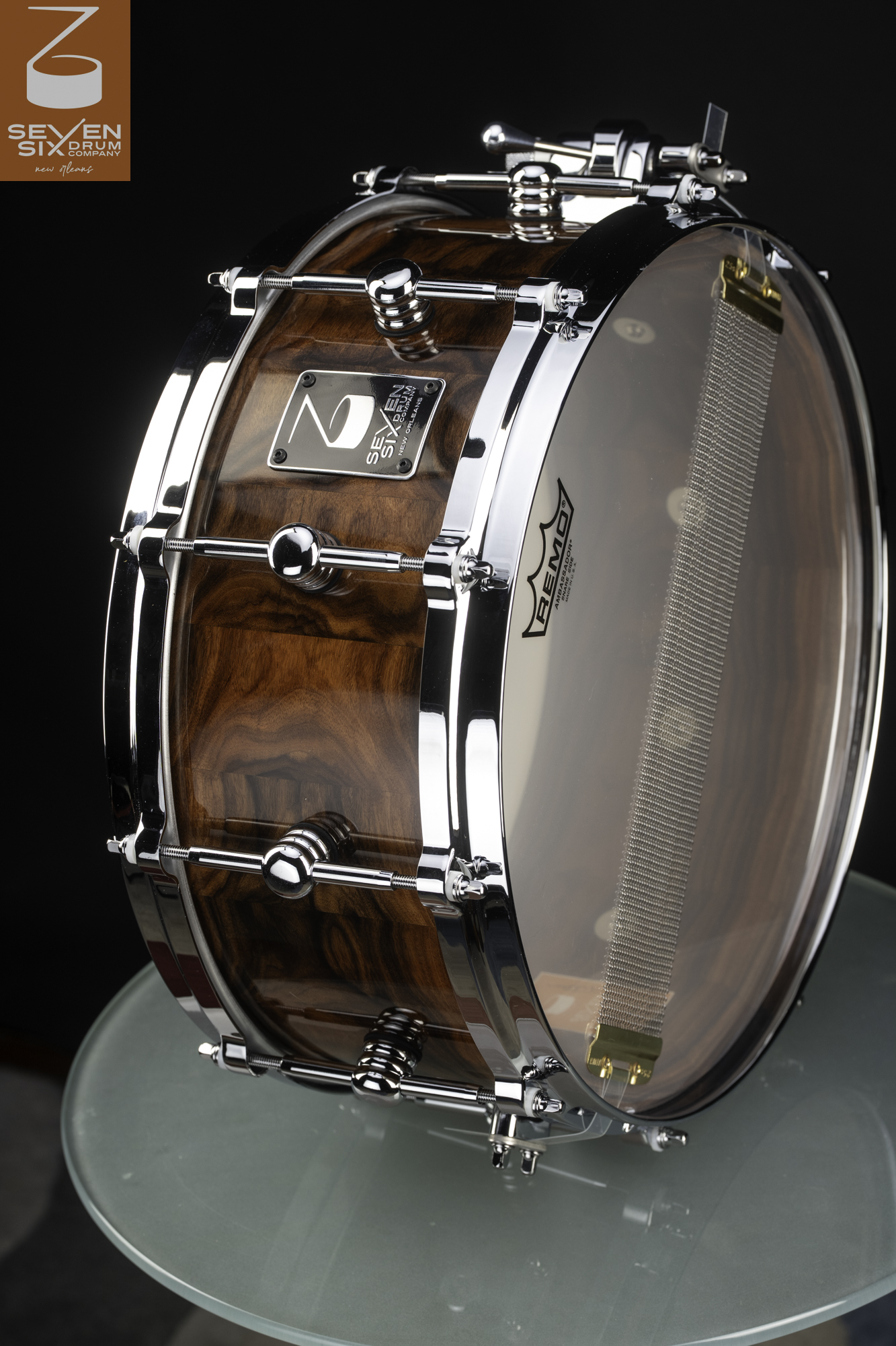 Handmade snare drum with a glossy wood grain shell, chrome hoops and center lugs, and a clear snare-side head.