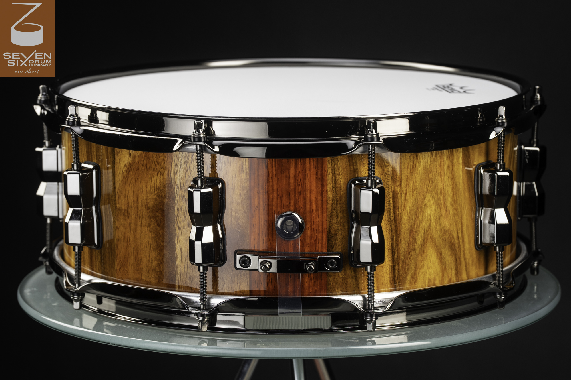 Handmade snare drum featuring a high-gloss striped wood shell accented with black nickel hoops and hardware.