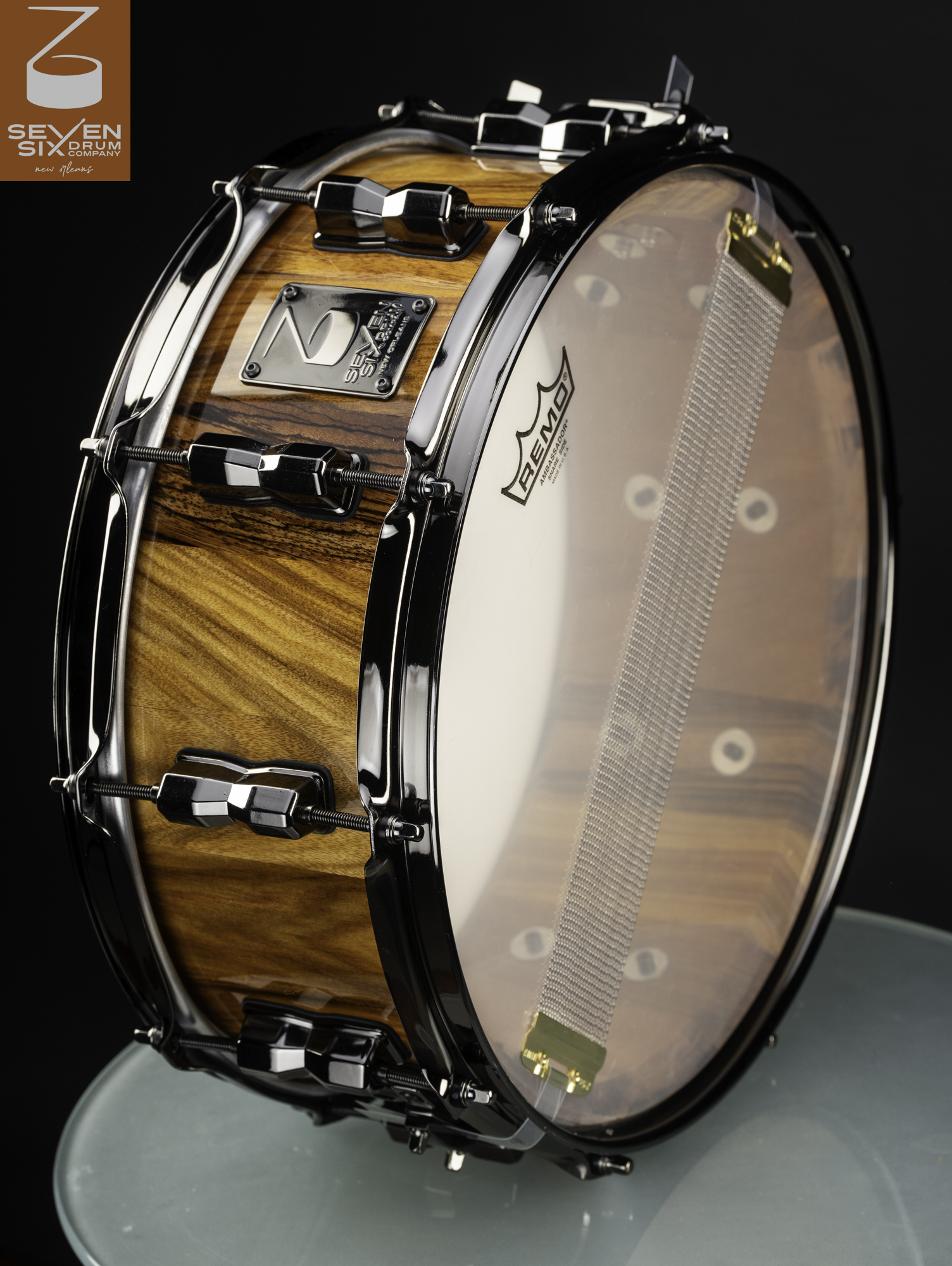 Handmade snare drum with a glossy striped wood shell, black nickel hardware, and a clear resonant head.