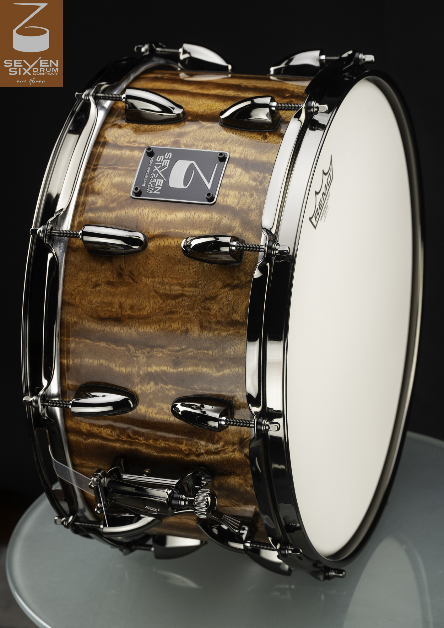 Handmade snare drum featuring a glossy figured amber wood shell, polished black nickel hoops, and teardrop lugs.