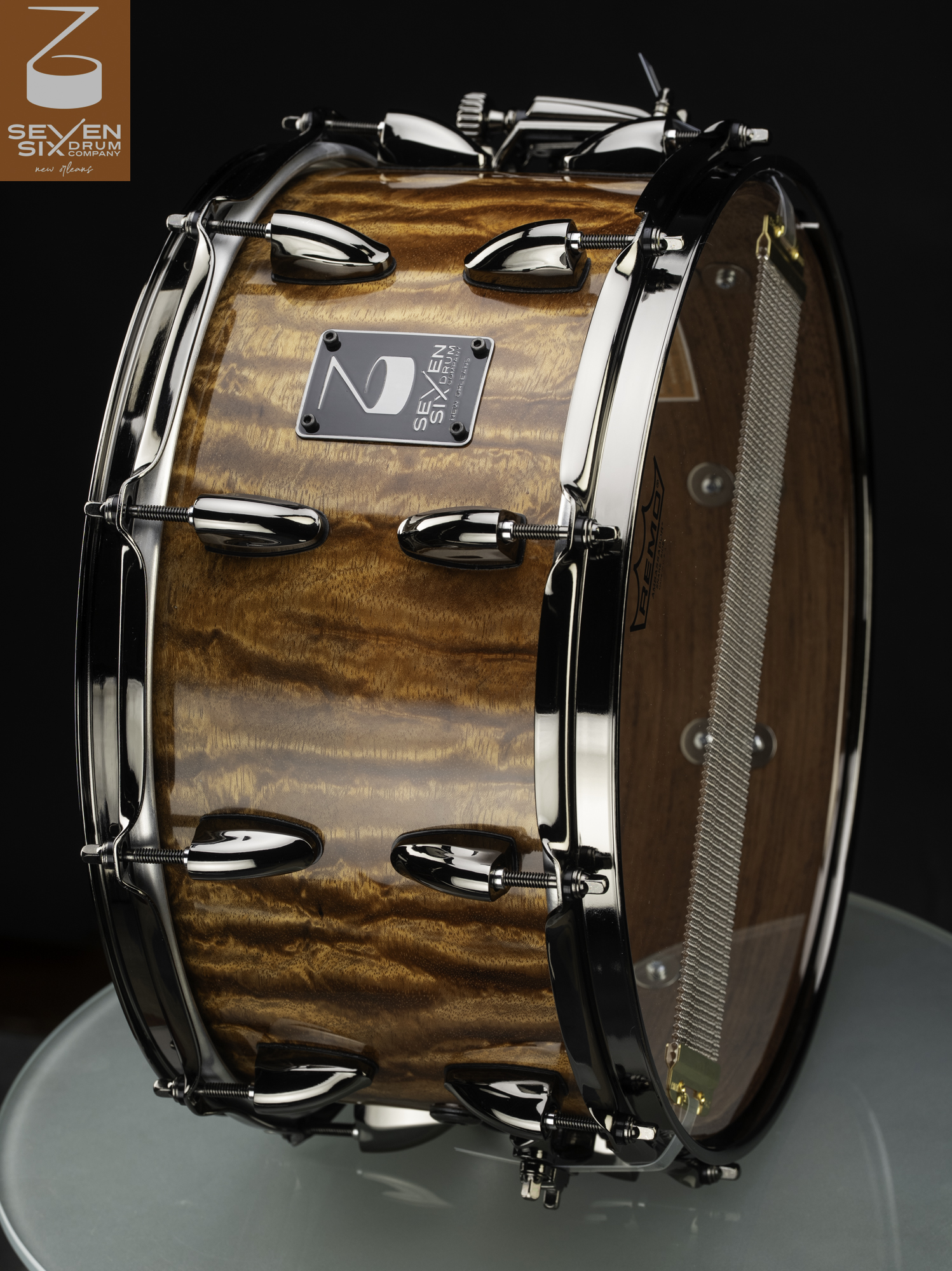 Handmade snare drum with a glossy figured wood shell, polished chrome hoops, bullet lugs, and snare wires.