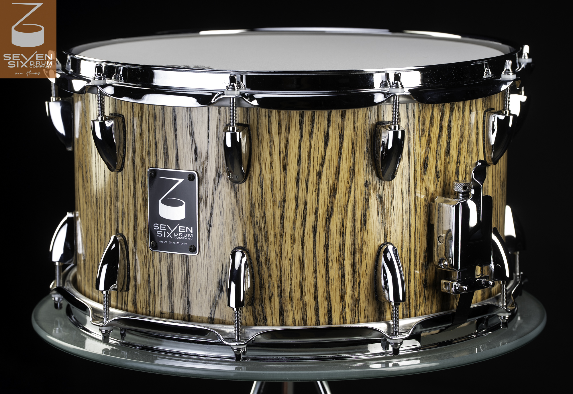 Wooden snare drum with a natural striped grain finish, fitted with polished chrome lugs, hoops, and strainer.