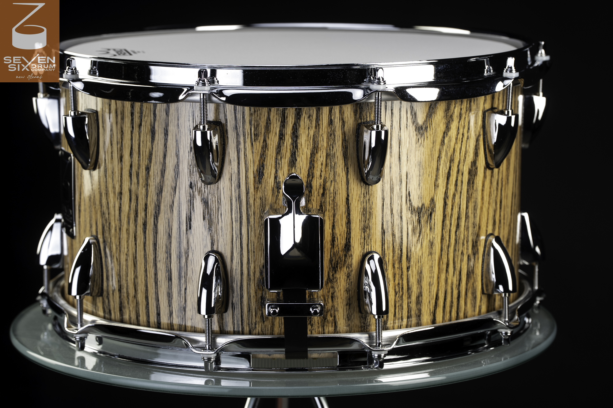 Handmade snare drum featuring a natural vertical wood grain finish, chrome hoops, bullet lugs, and a polished throw-off.