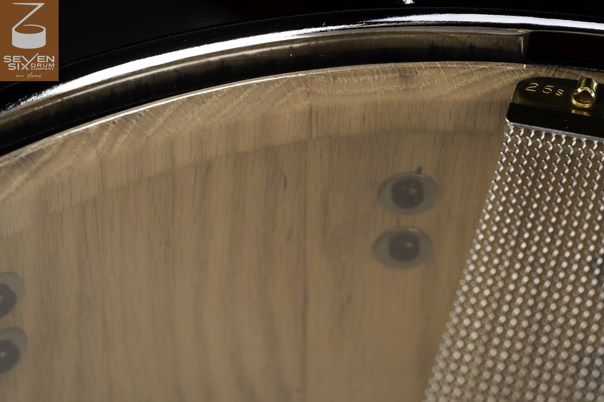 Natural wood snare drum interior viewed through a clear resonant head, featuring a chrome hoop and brass snare wires.