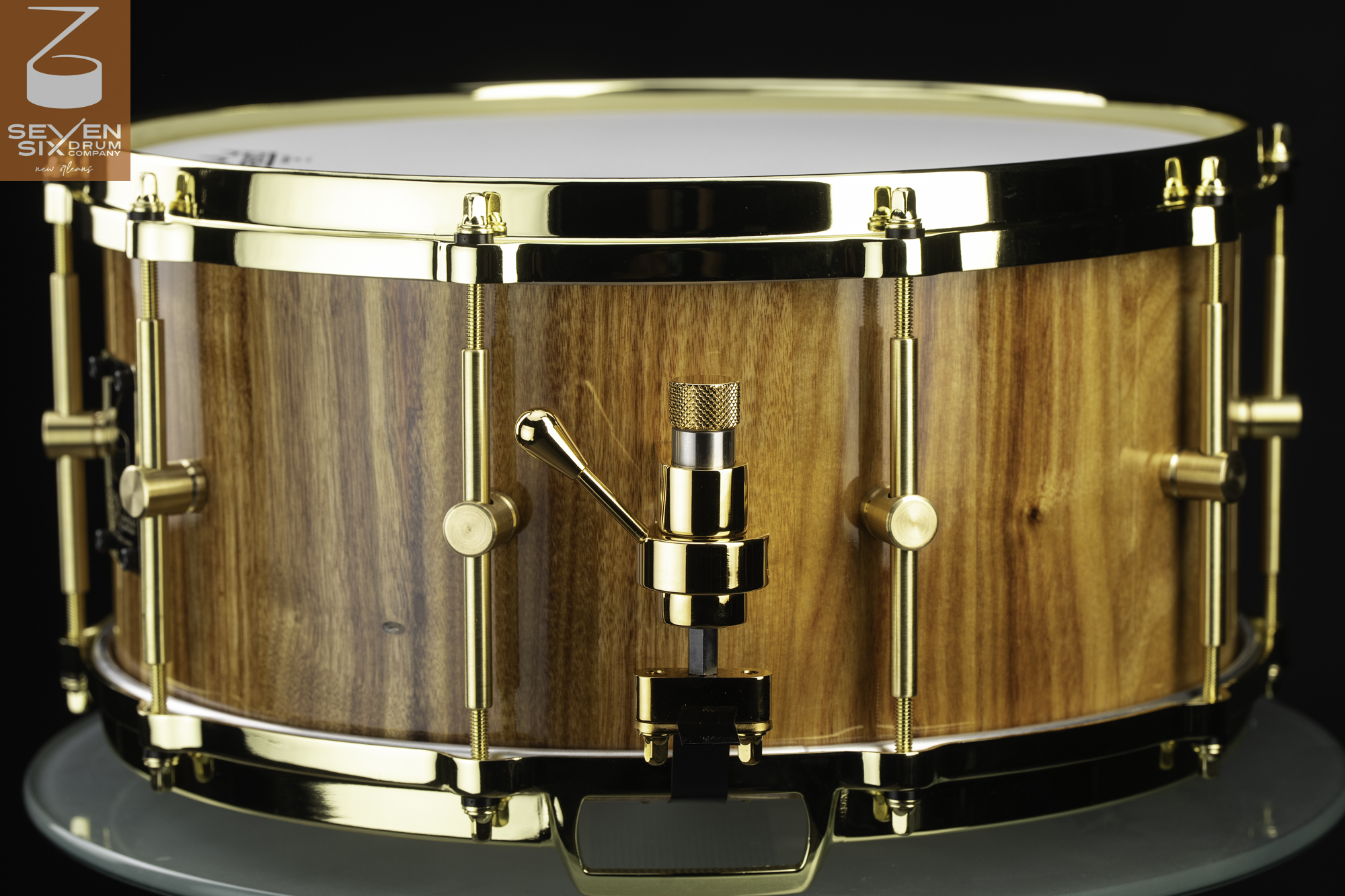 Handmade snare drum featuring a glossy natural wood shell with polished gold hoops, tension lugs, and a matching snare throw-off.