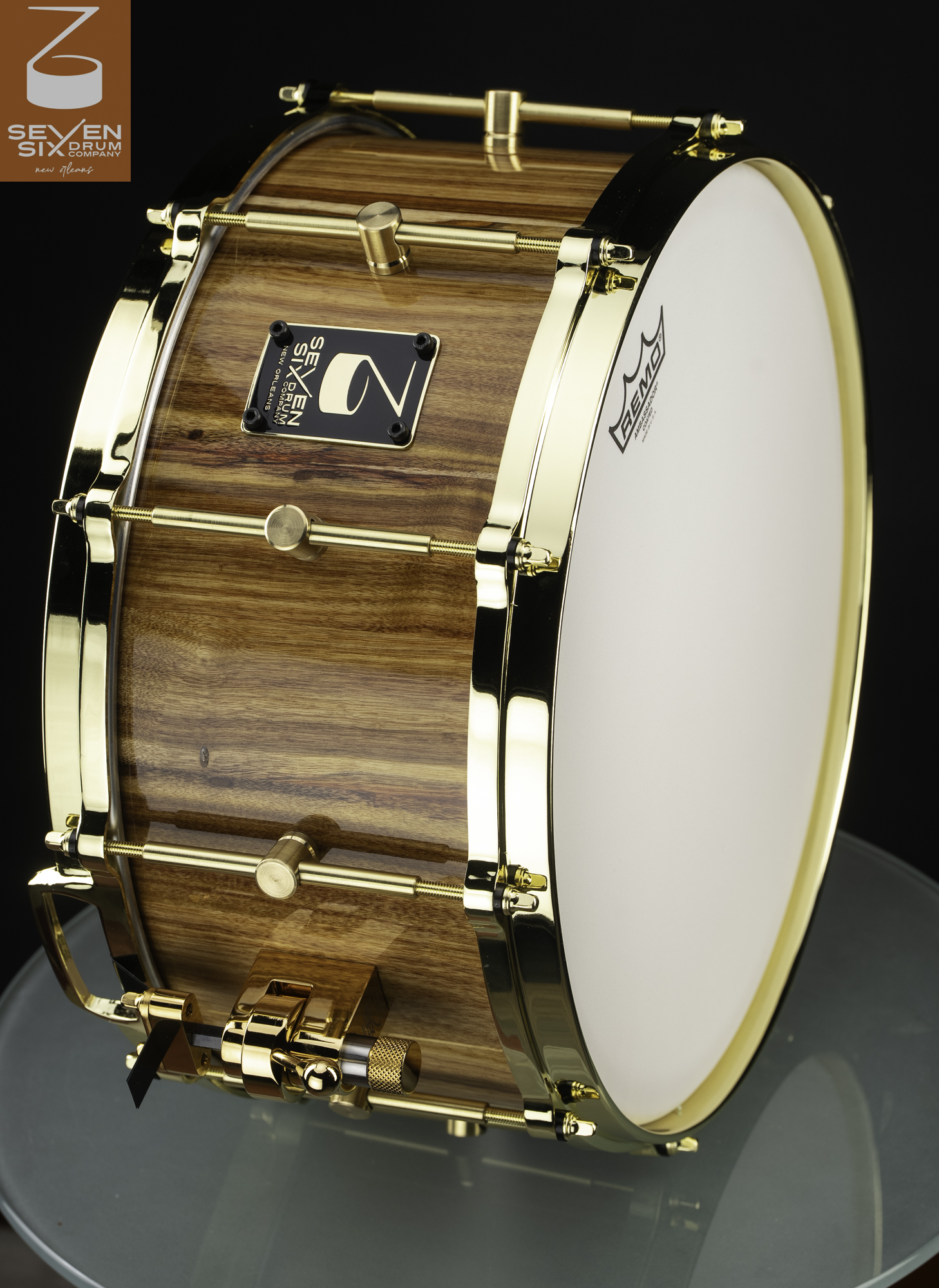 Handmade snare drum featuring a glossy natural wood shell with polished gold hoops and tube lugs.