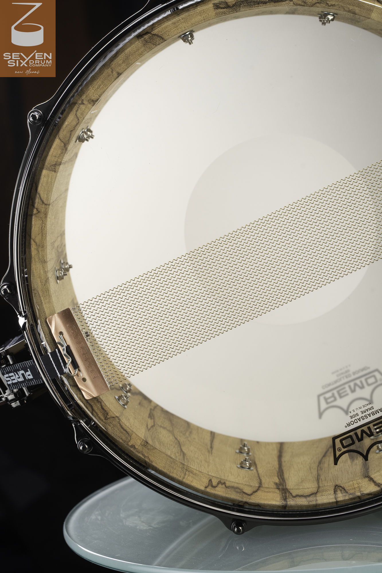 Bottom of a snare drum with a natural figured wood shell interior, chrome hoop, and PureSound snare wires across the head.