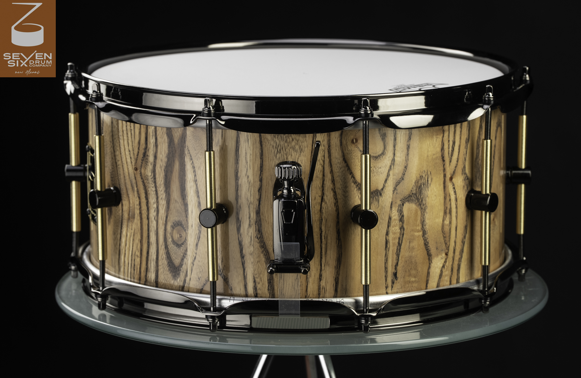 Handmade snare drum with a natural wood grain shell, black nickel hoops and throw-off, and brass tube lugs.