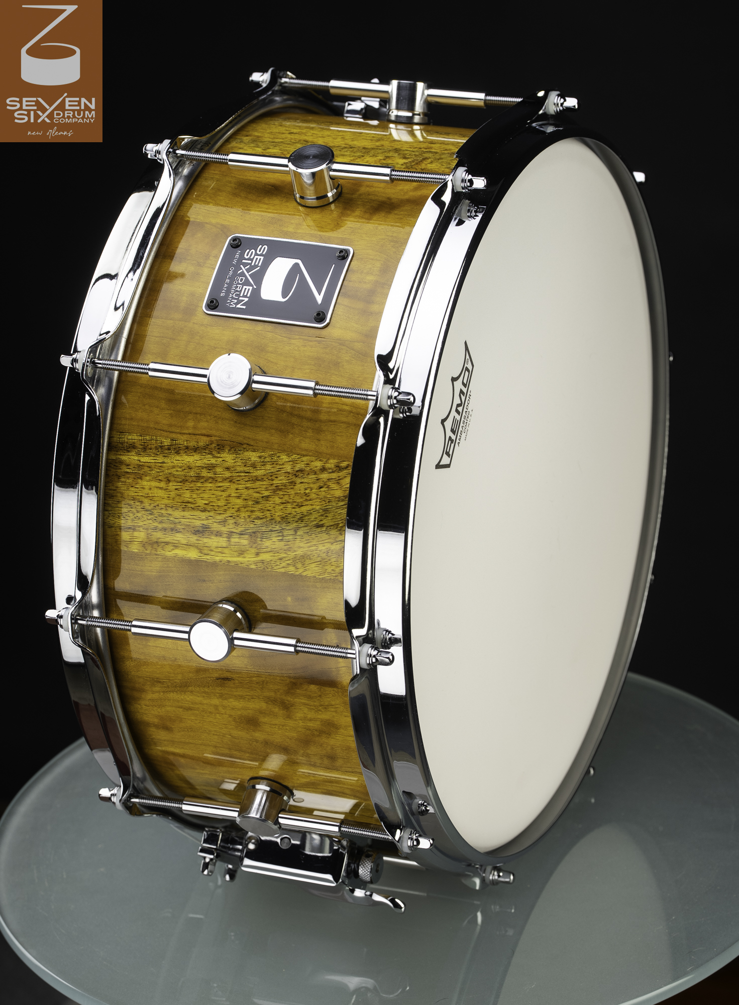 Handmade snare drum with a glossy amber wood shell, polished chrome hoops, and round center-mounted lugs.