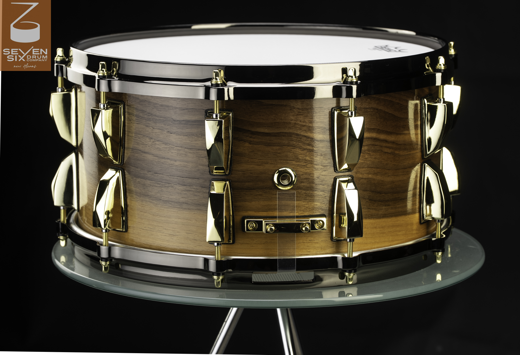 Handmade snare drum with a glossy wood finish, polished gold lugs, and black chrome hoops.