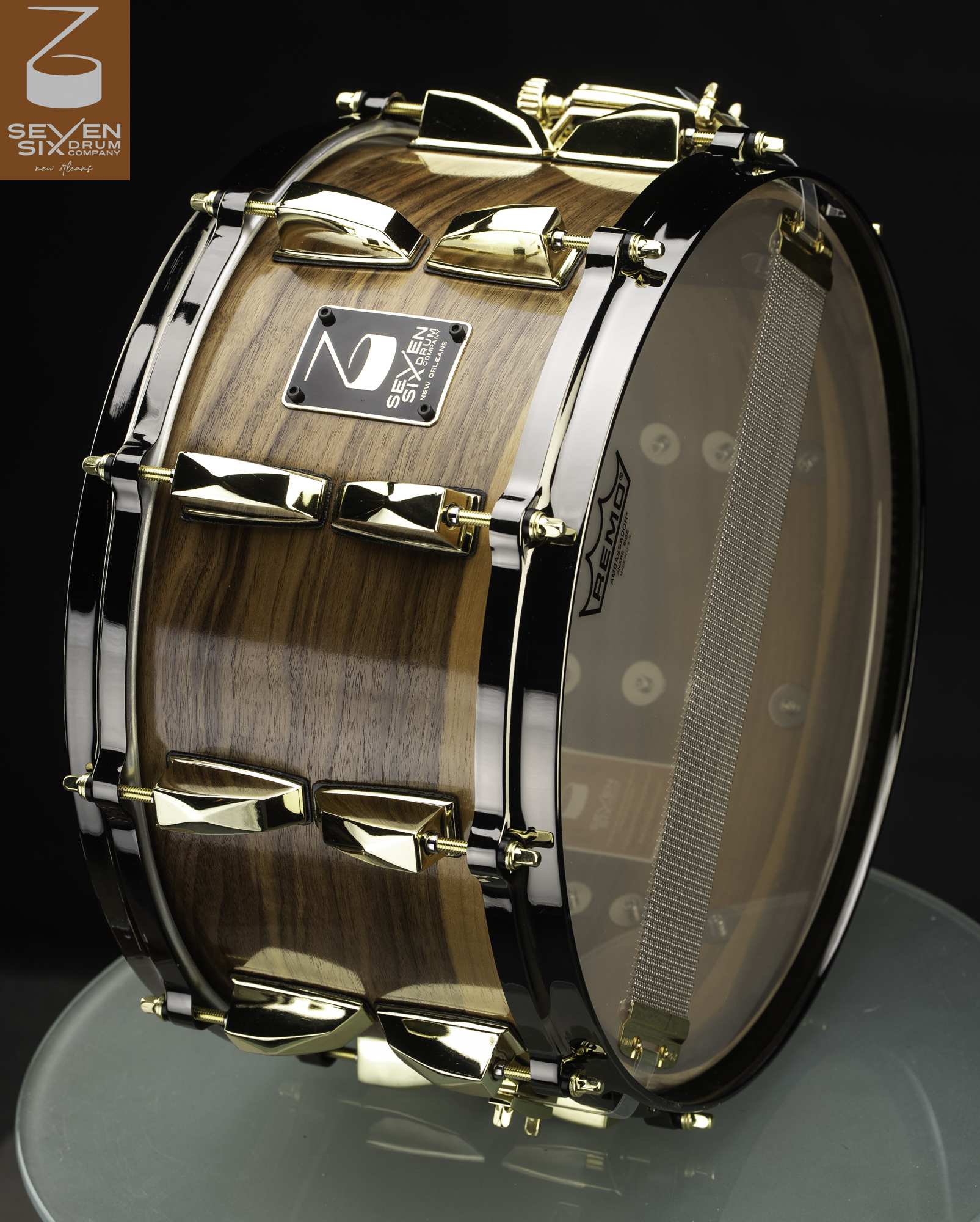 Glossy natural wood snare drum with polished gold lugs, brass tension rods, and black nickel hoops.