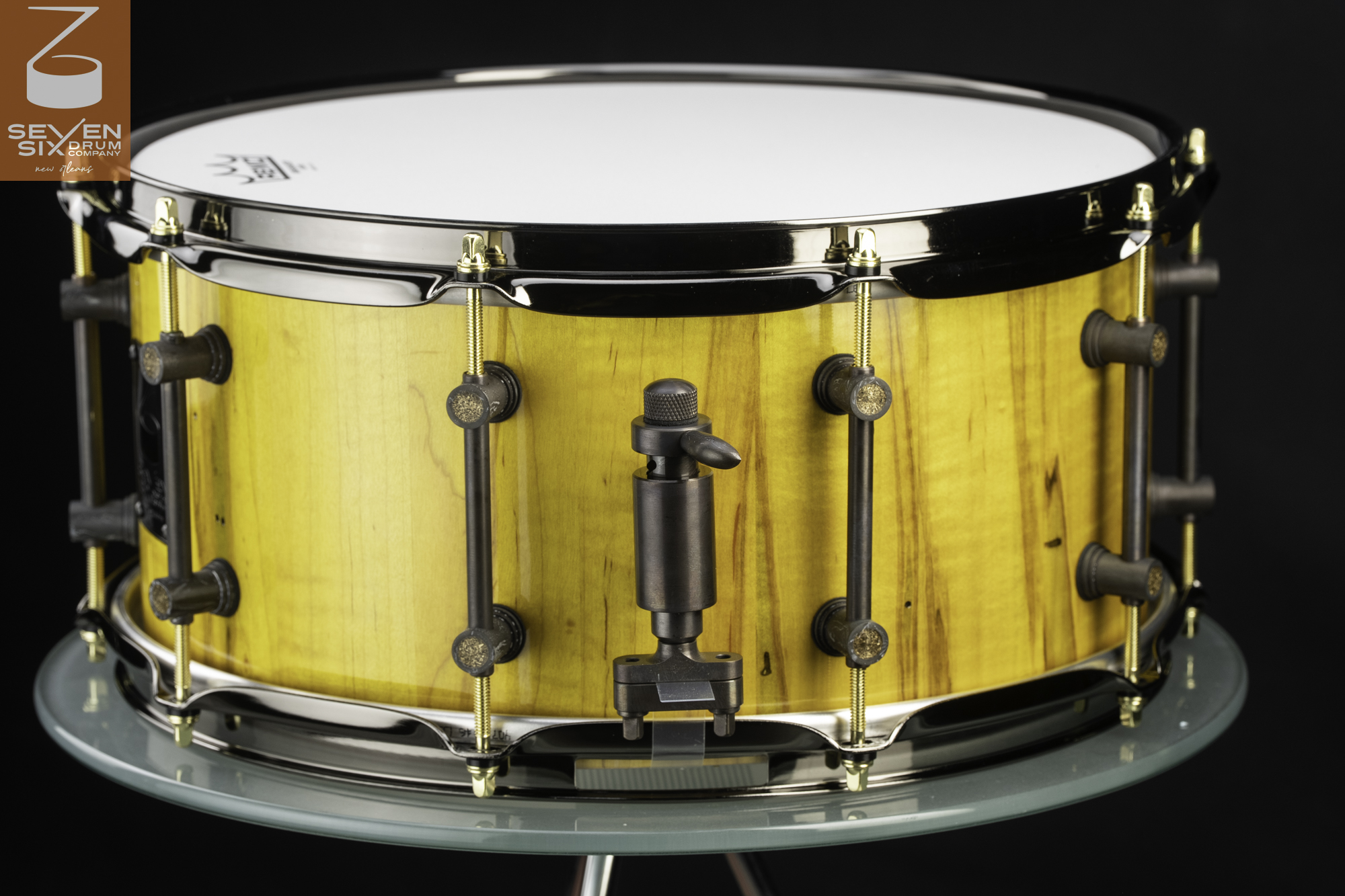 Handmade snare drum with a glossy yellow wood shell, dark bronze hardware, brass tension rods, and polished metal hoops.