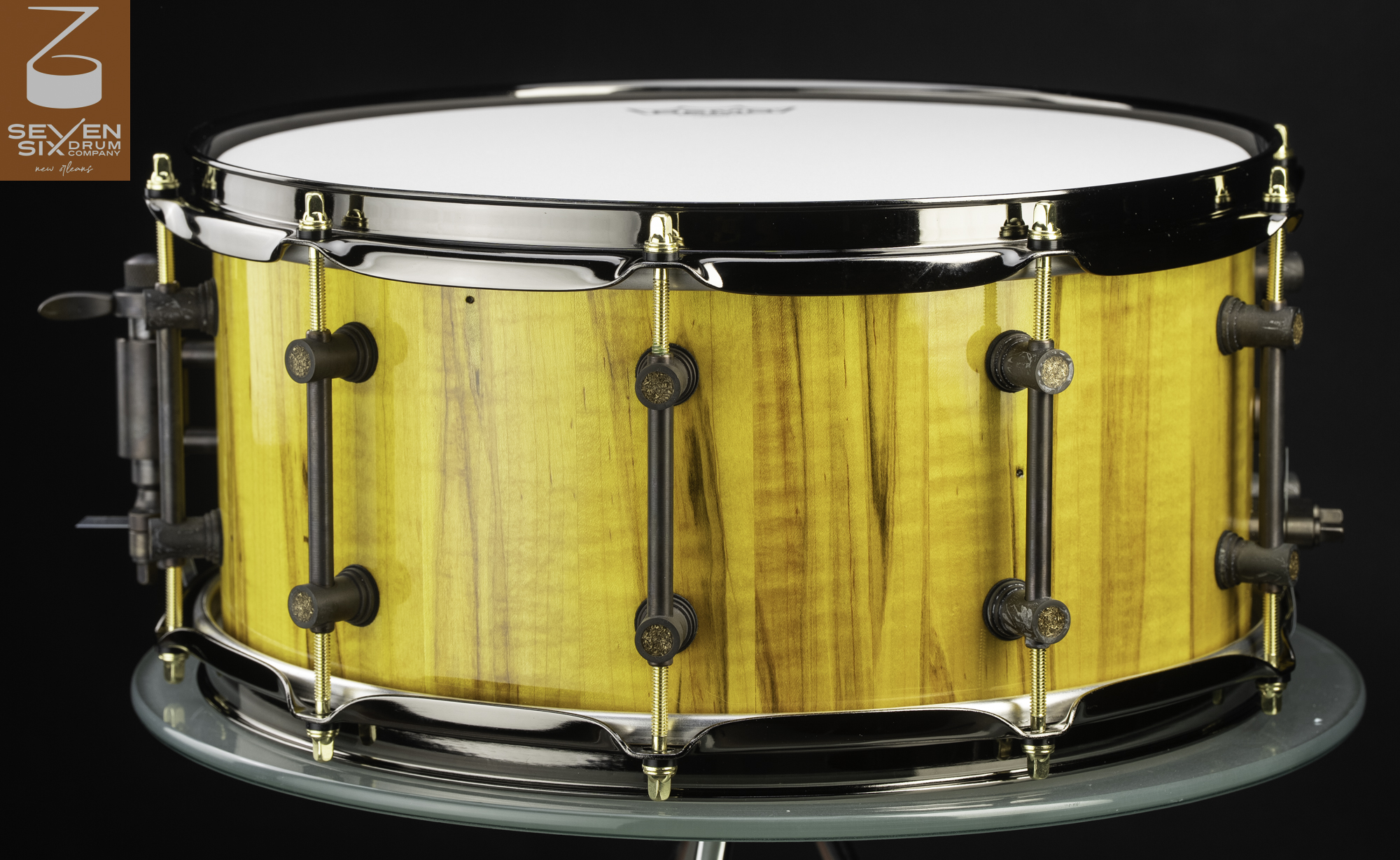 Handmade snare drum with a gloss yellow wood shell, dark bronze tube lugs, gold tension rods, and black nickel hoops.