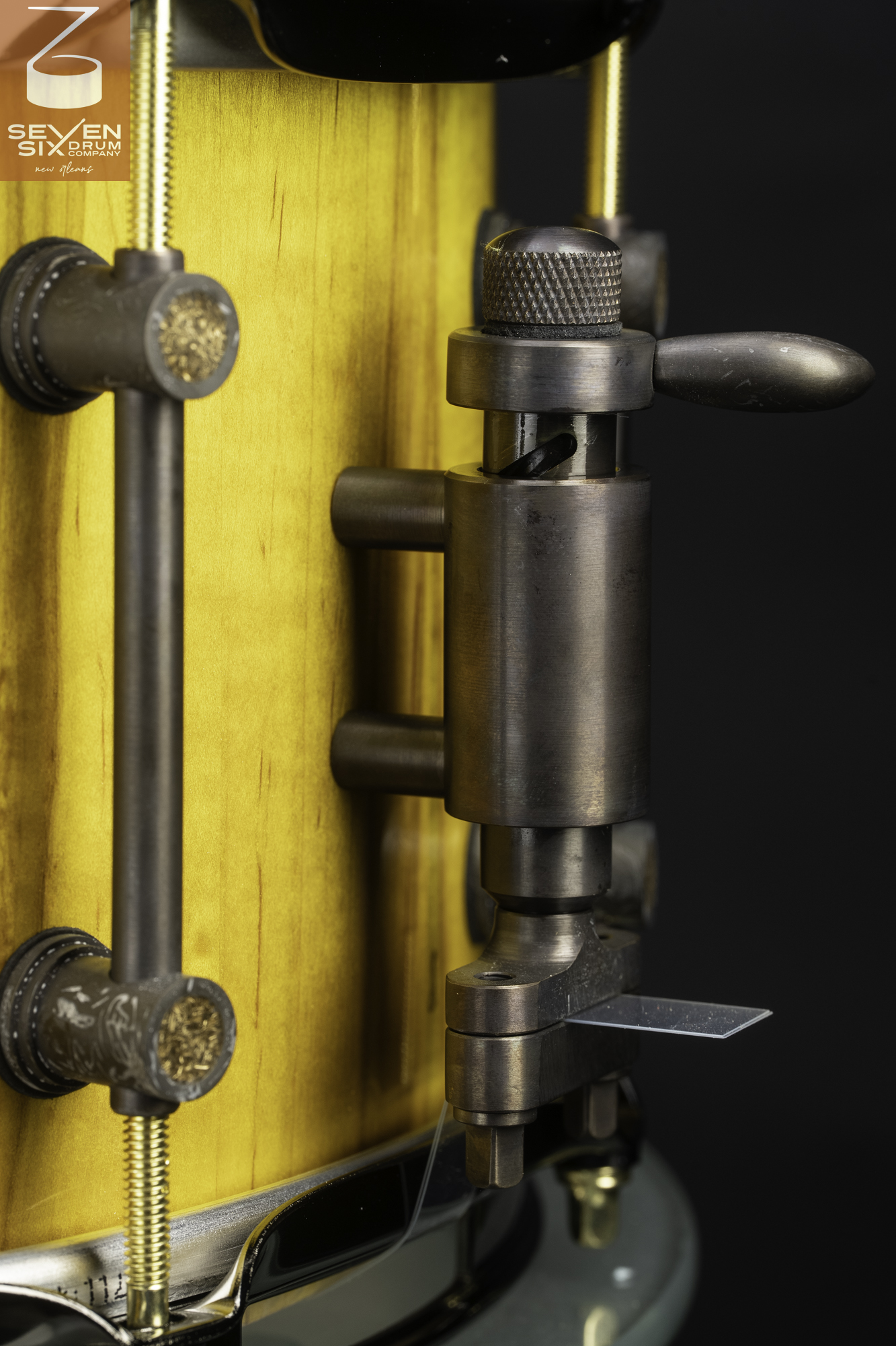 A yellow-stained wood snare drum featuring an antique bronze snare throw-off and matching tube lugs.