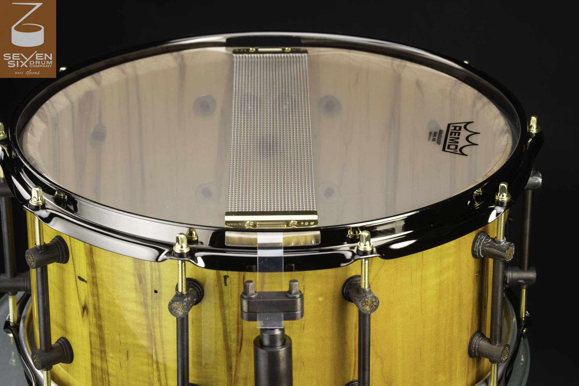 Handmade gloss yellow wood snare drum with a clear snare-side head, wire snares, black chrome hoop, and bronze tube lugs.
