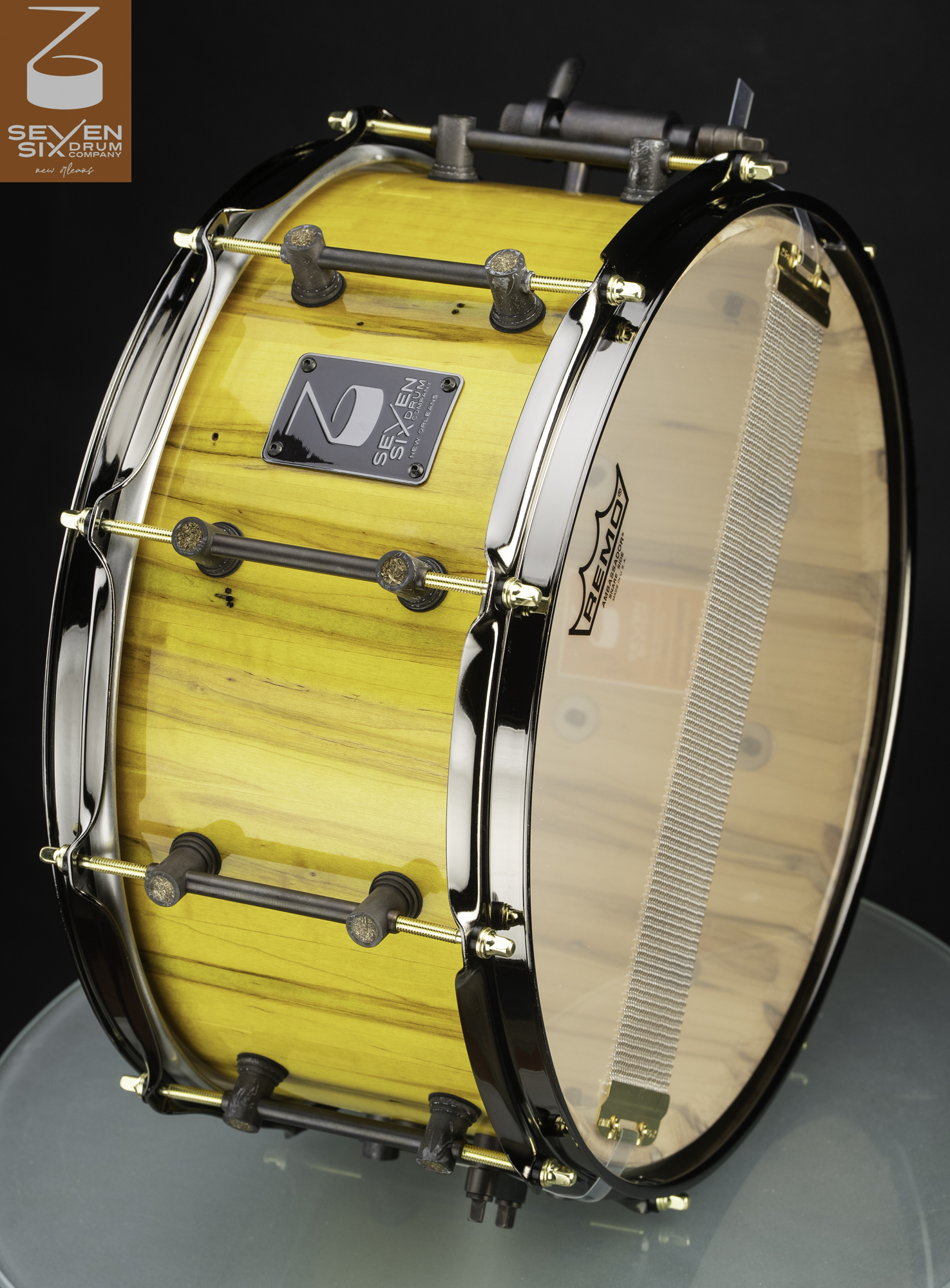Handmade snare drum with a glossy yellow wood shell, dark tube lugs, brass tension rods, and polished chrome hoops.