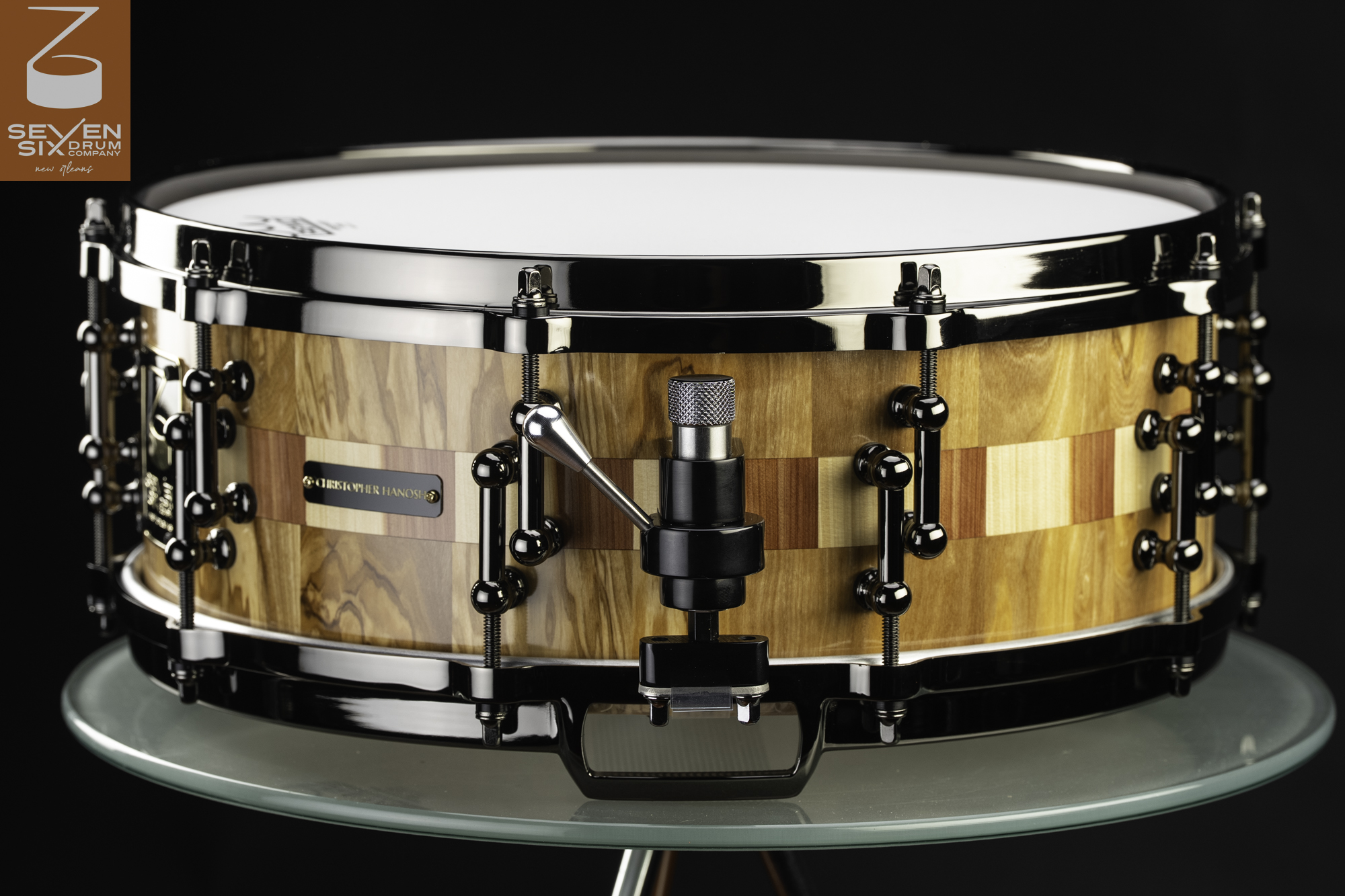 Handmade segmented wood snare drum with a gloss finish, checkered inlay, and black nickel hardware.