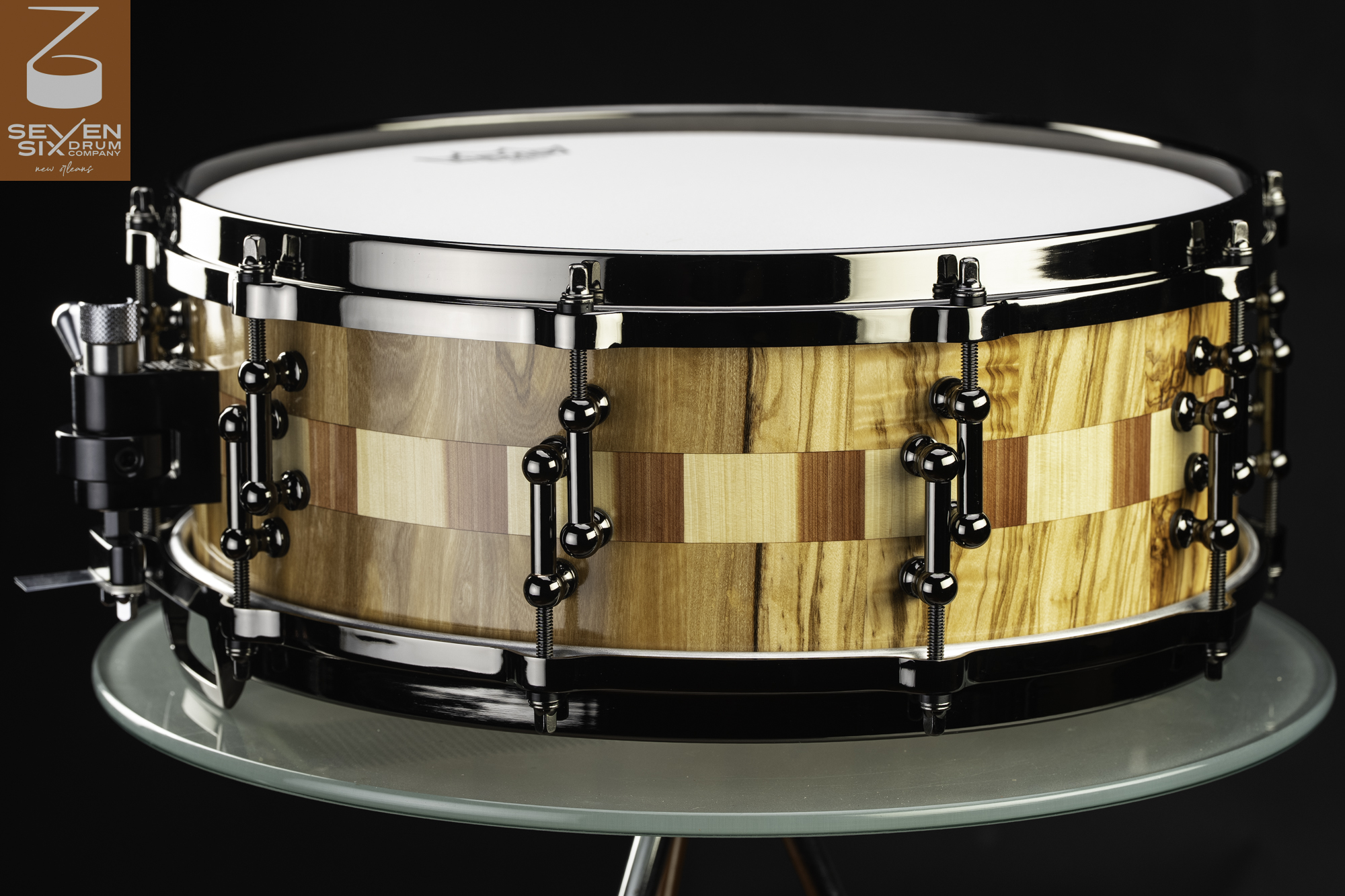 Handmade snare drum featuring a segmented natural wood shell with a gloss finish and black nickel lugs and hoops.