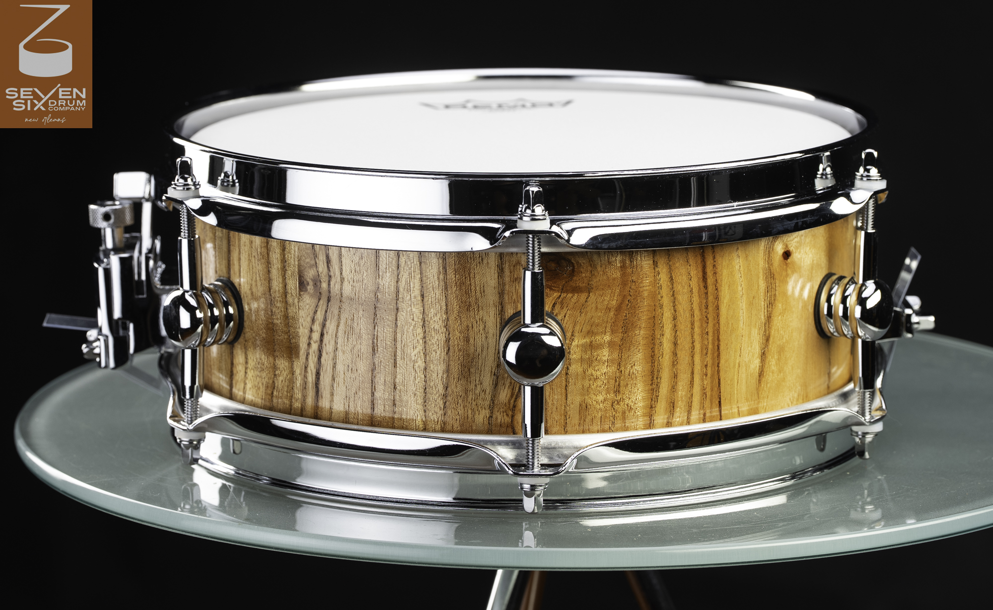 Handmade snare drum featuring a natural gloss wood shell, polished chrome hoops, and rounded center lugs.