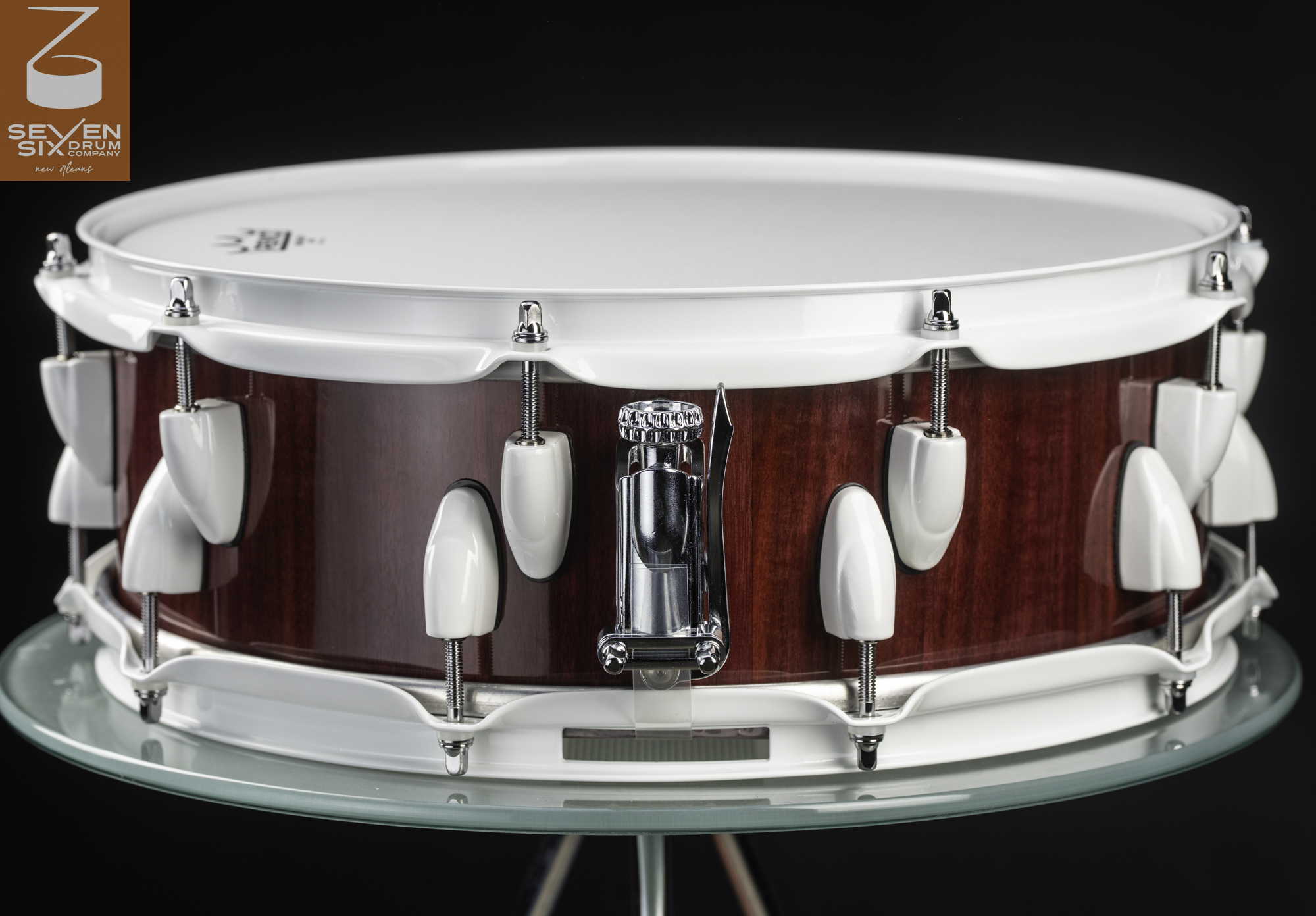Handmade snare drum featuring a glossy red wood shell, white rims and lugs, and a chrome throw-off.