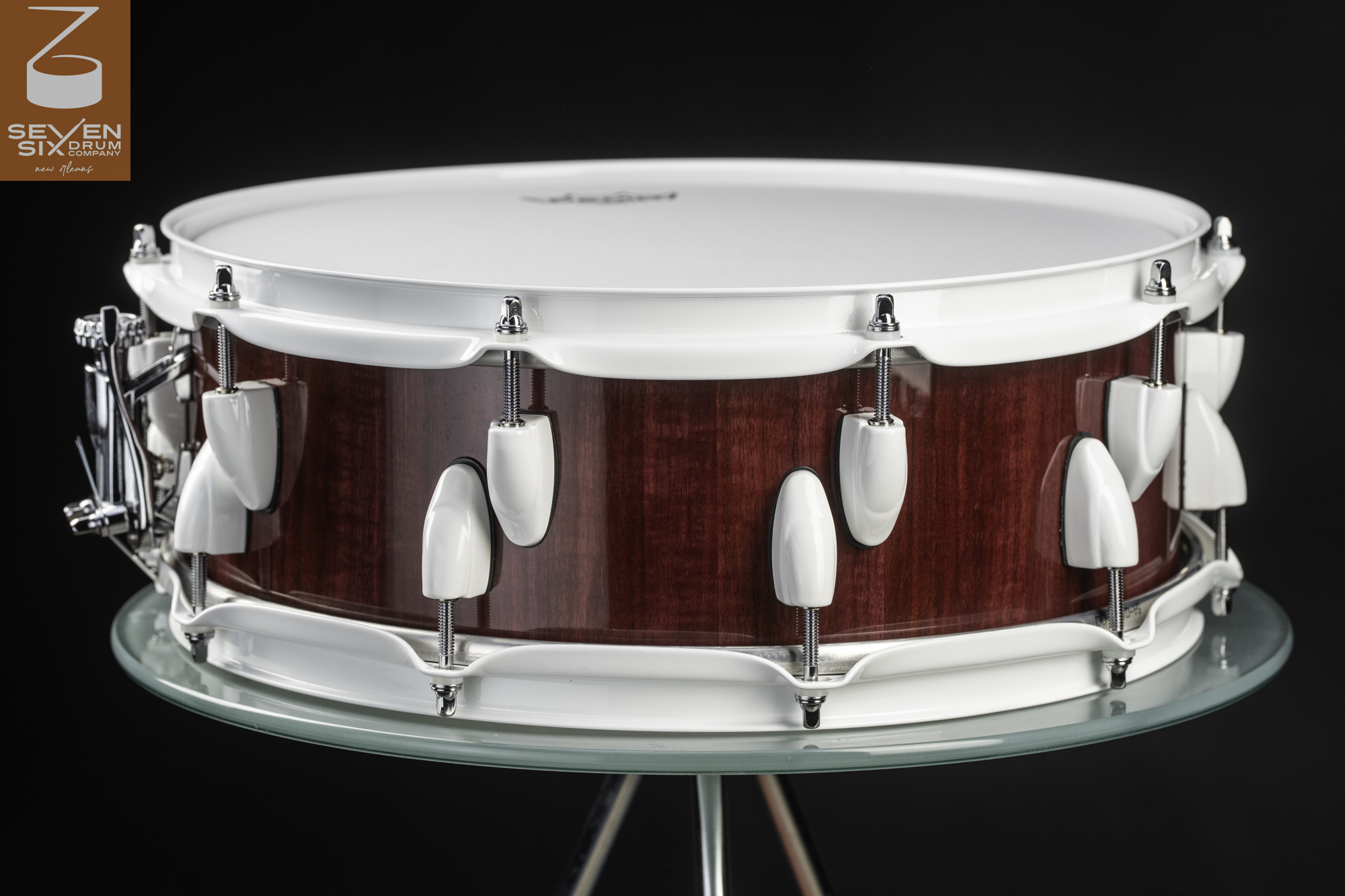 Handmade snare drum featuring a glossy red-stained wood shell, white hoops, and white lugs with chrome accents.